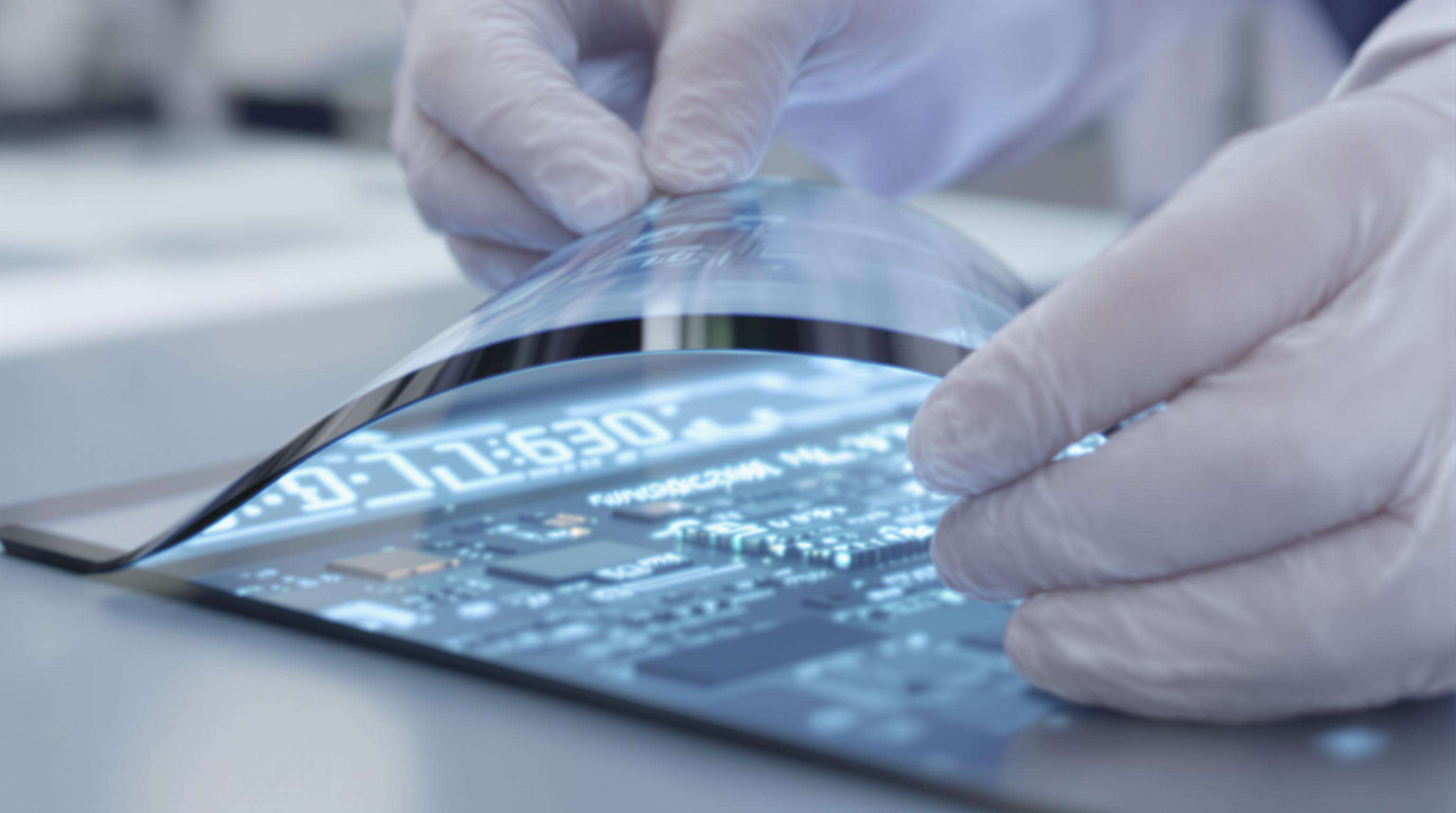 Gloved hands bending a flexible OLED display with visible micro-electronics in a lab setting