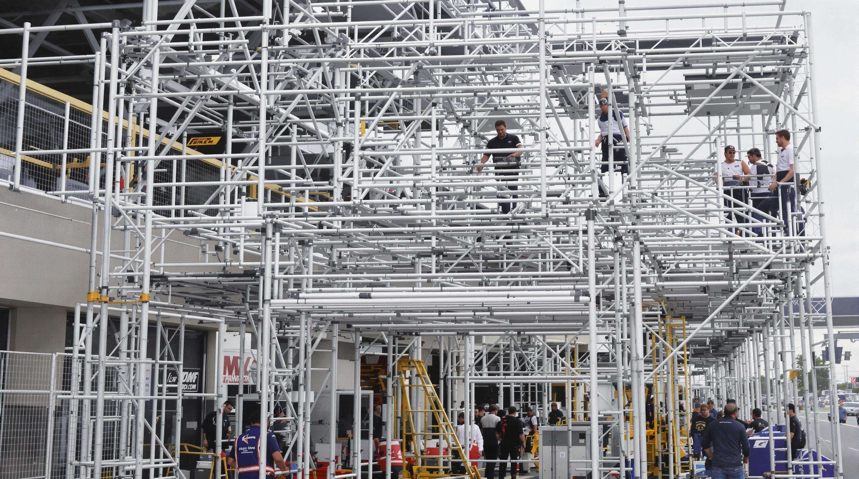 Realistic photo of motorsport crew assembling modular aluminum truss grandstand and media platform on uneven terrain, highlighting precision connectors and versatility.