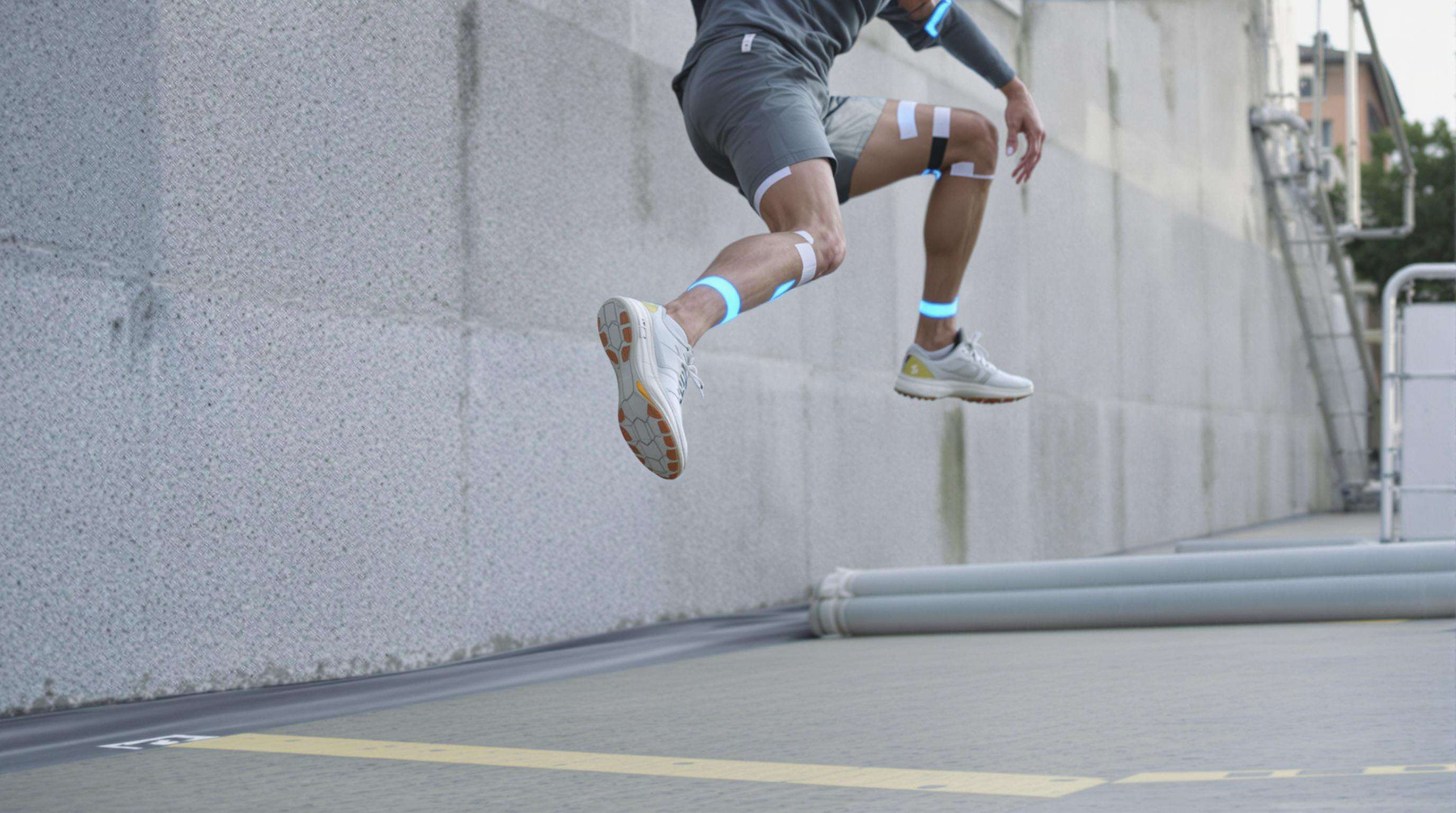 Close-up of a parkour athlete jumping from wall to ground with motion markers, landing safely on a rubberized surface