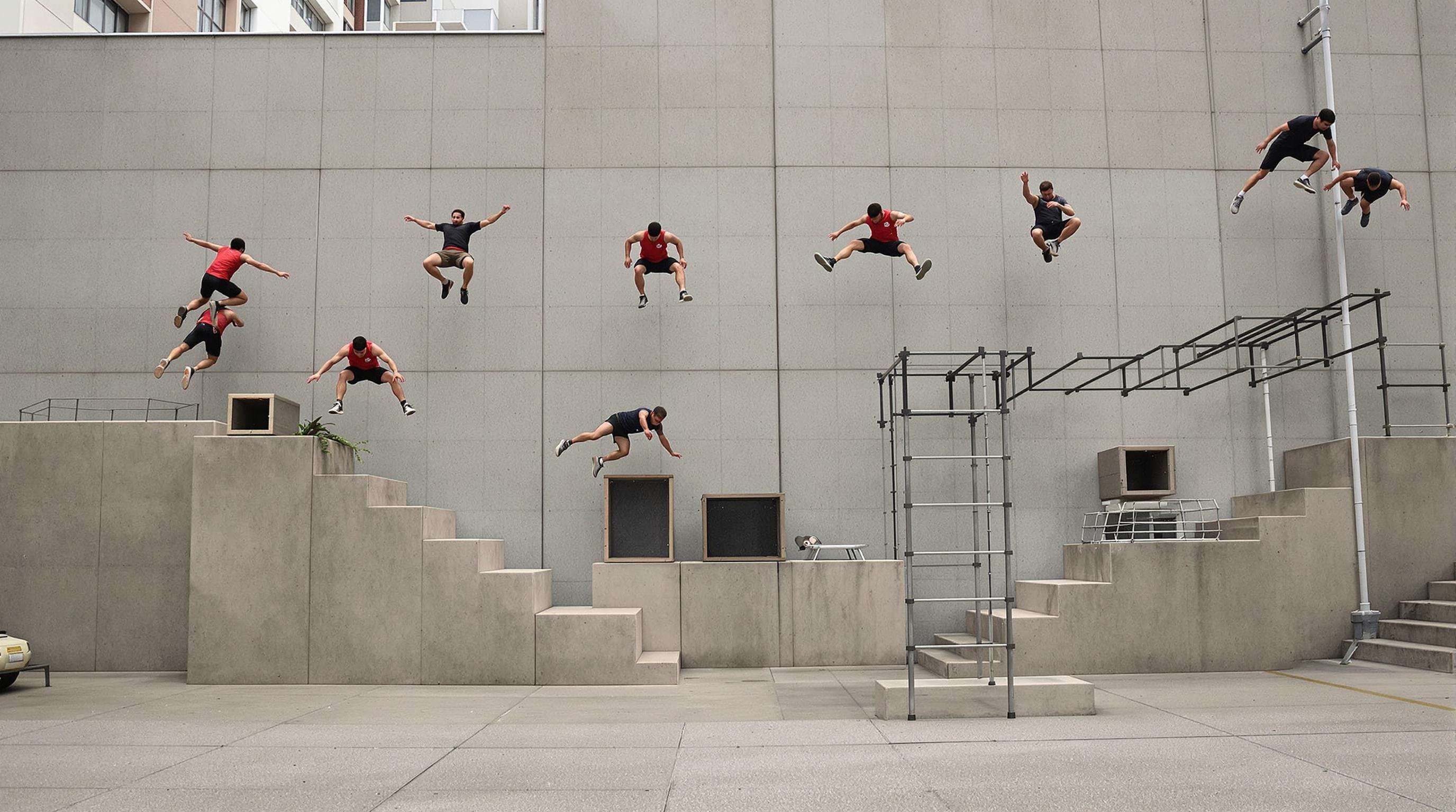 Parkour athletes moving fluidly between angled walls, vault boxes, and bars in an open training space