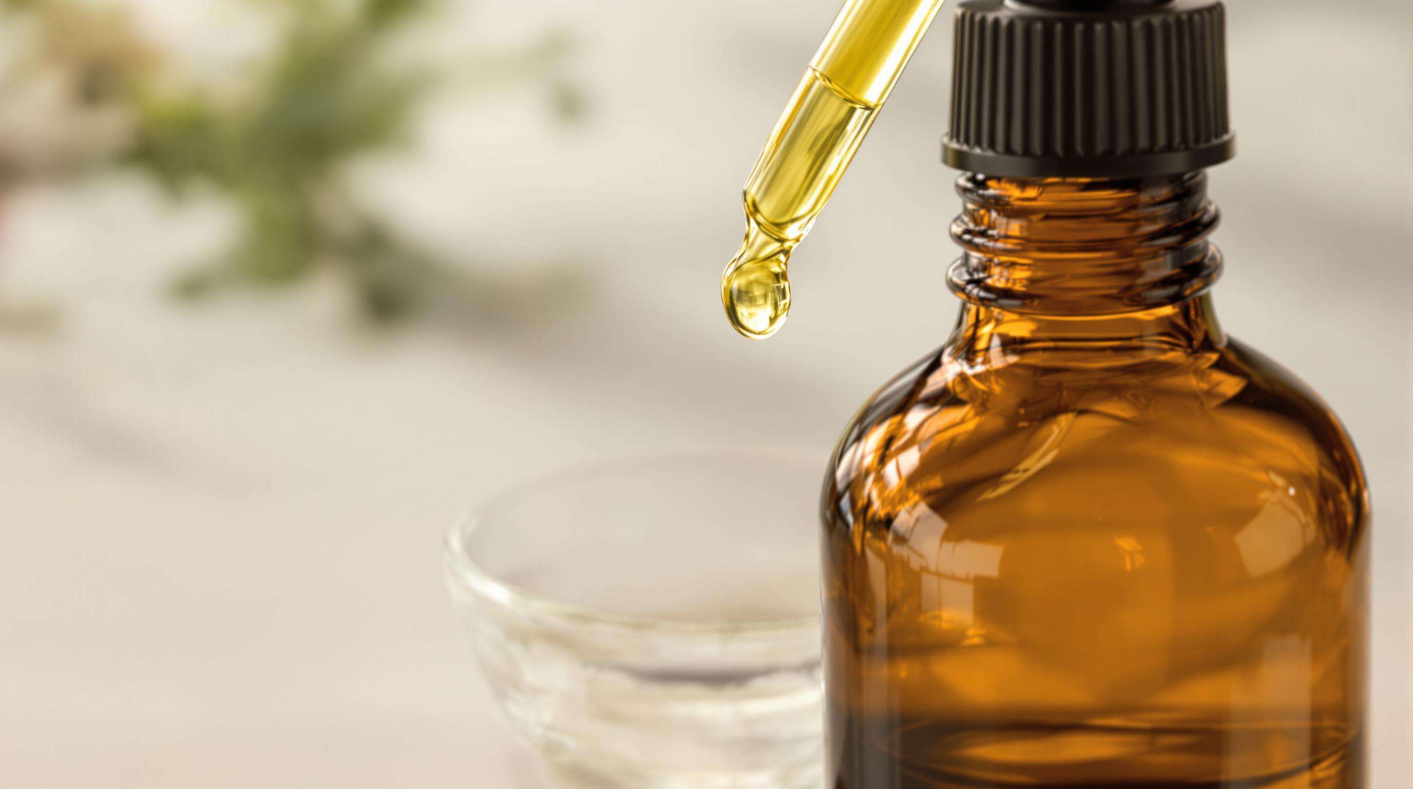 Close-up of an amber glass bulk essential oil bottle using an integrated dropper to dispense oil into a small dish