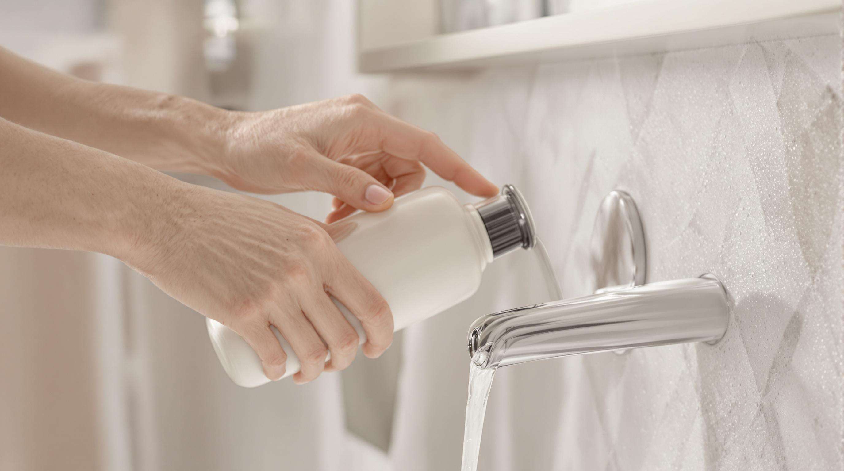 Refillable matte glass lotion bottle being refilled in a modern bathroom, highlighting ergonomic and magnetic design features