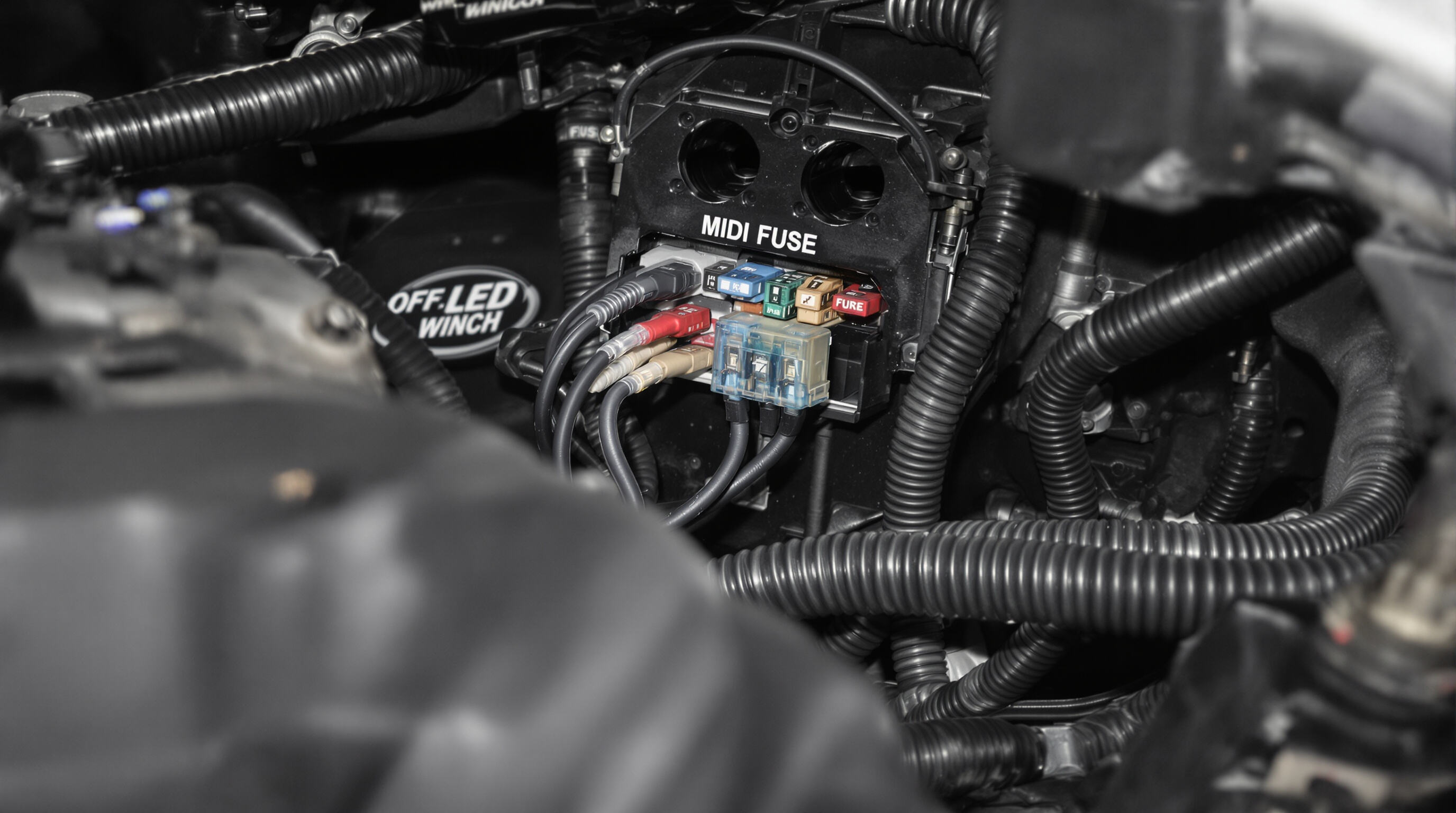Photograph of an engine bay showing a midi auto fuse with thick cables connected to high-power accessories like a winch and LED light bar.