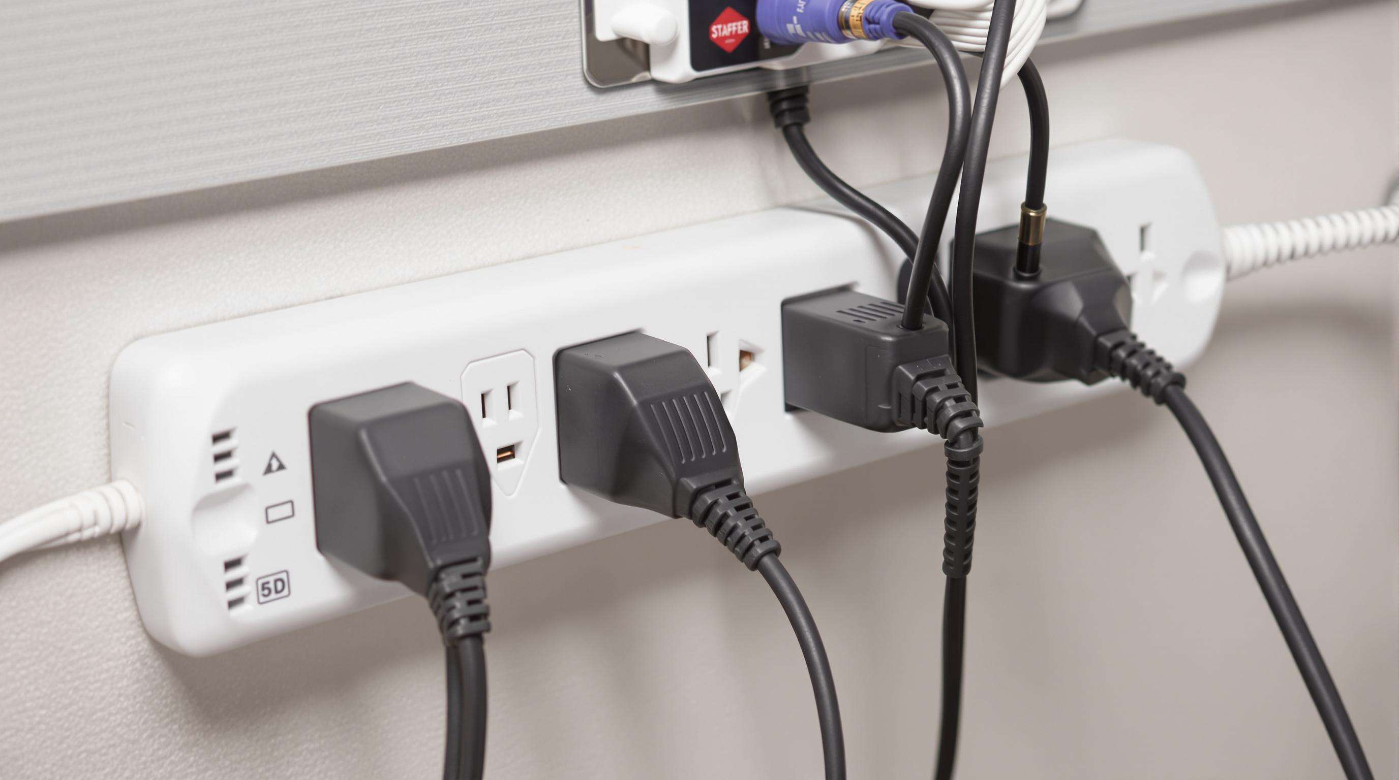 Adapters plugged into a surge protector with thick cables in a muted color office setup