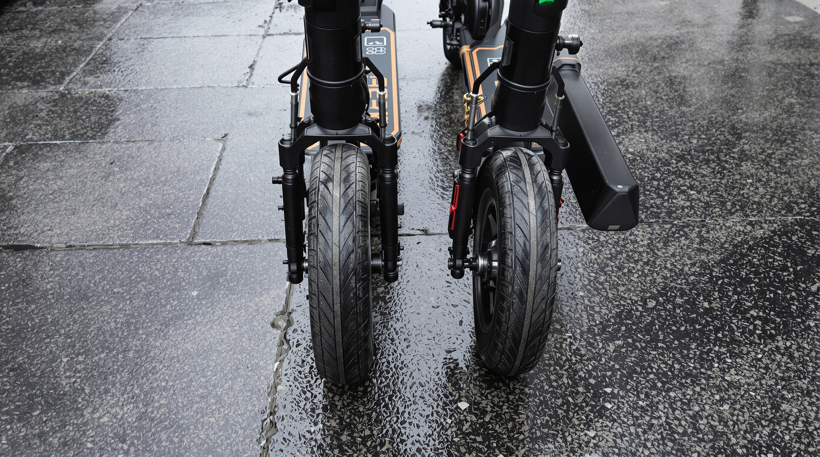 Side-by-side scooters on wet pavement showing puncture-proof versus pneumatic tires for performance comparison.