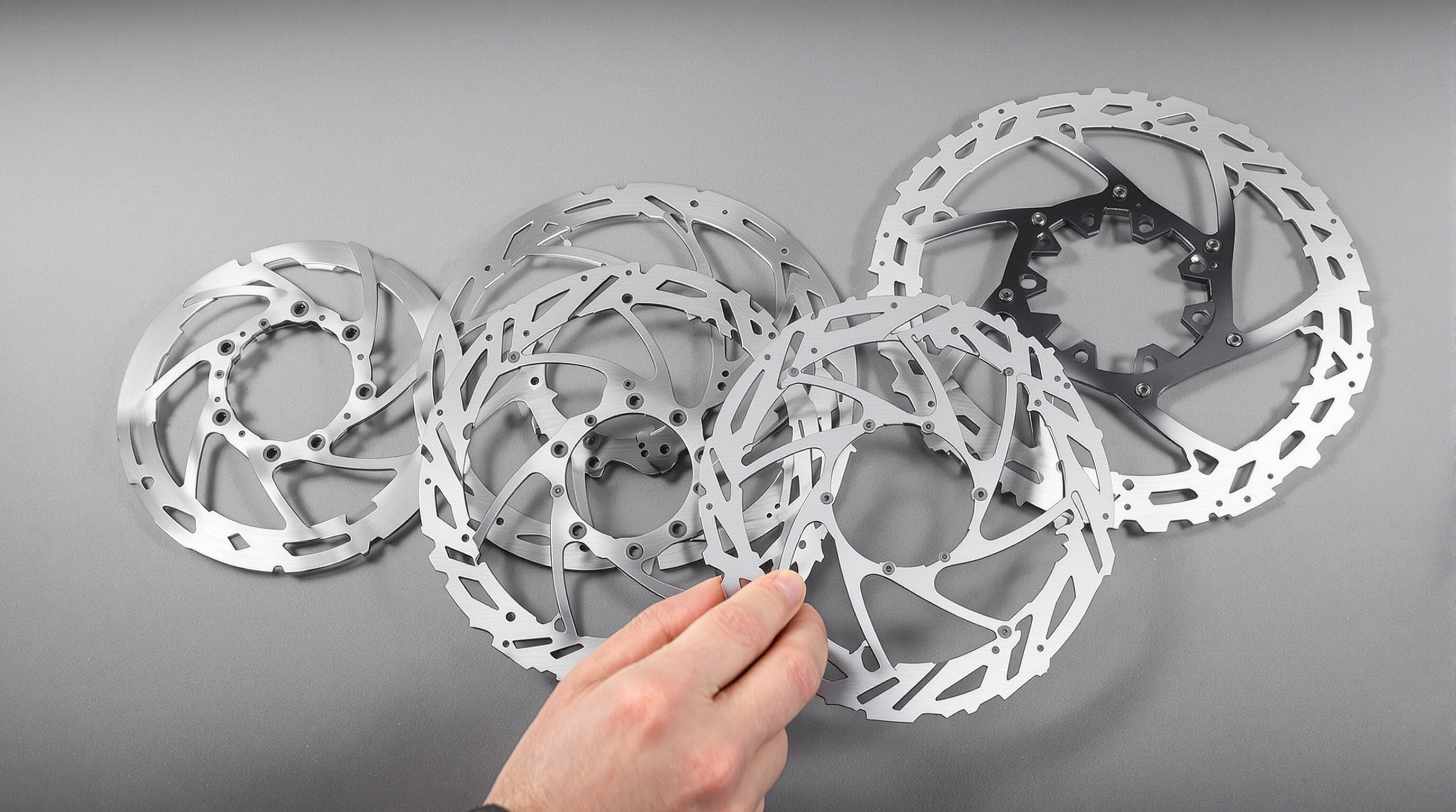 Assorted sizes of e-bike disc brake rotors displayed on a workbench with a hand reaching for the largest one