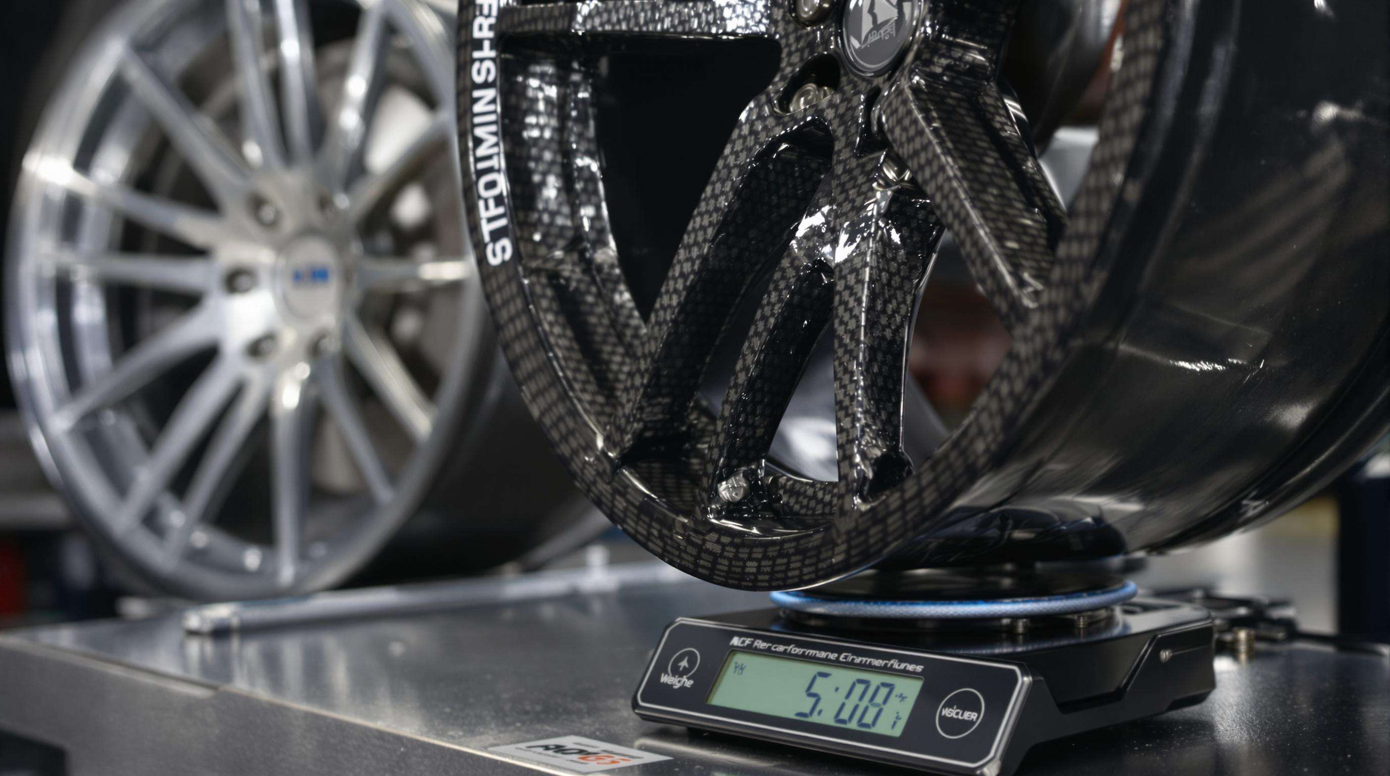 Photorealistic close-up of a carbon fiber car wheel being weighed with an aluminum wheel visible in the background