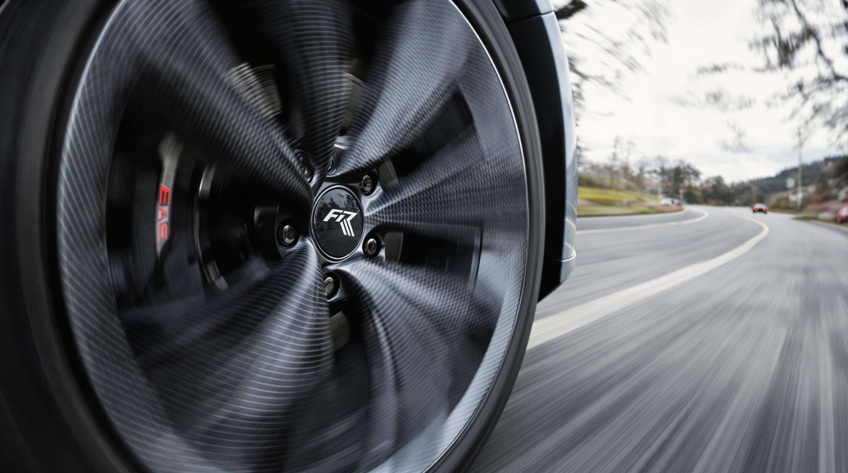 Close-up photo of a carbon fiber car wheel spinning on a road, emphasizing detail and motion