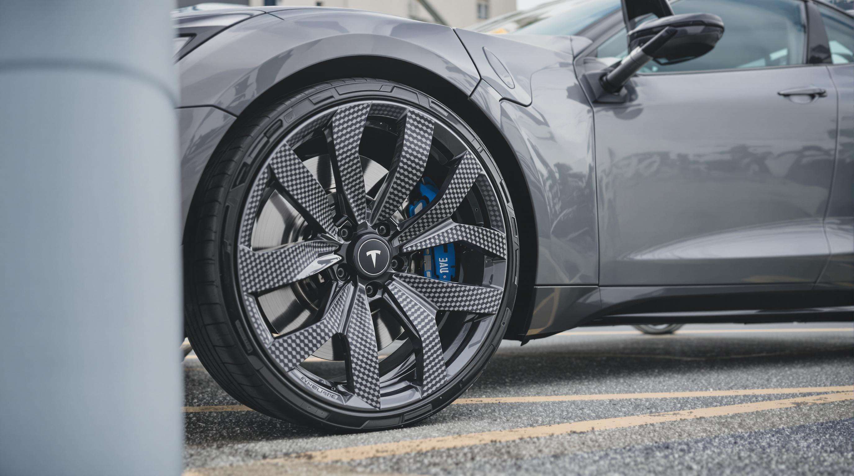 Electric vehicle at a charging station highlighting its carbon fiber wheels in an urban setting