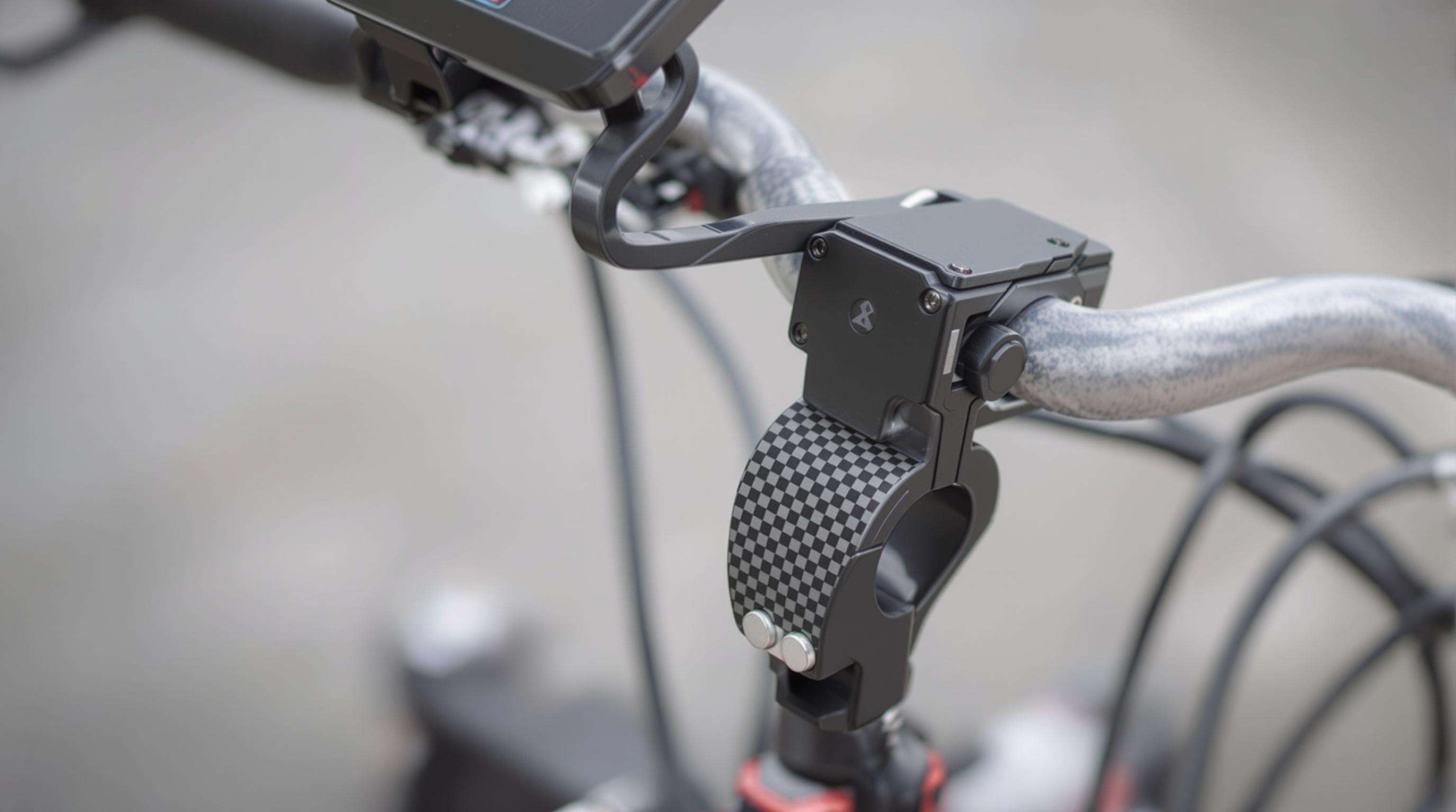 A photorealistic close-up of a dual-use selfie stick clamp mounted on bicycle and motorcycle handlebars, highlighting silicone grips and secure lock features.