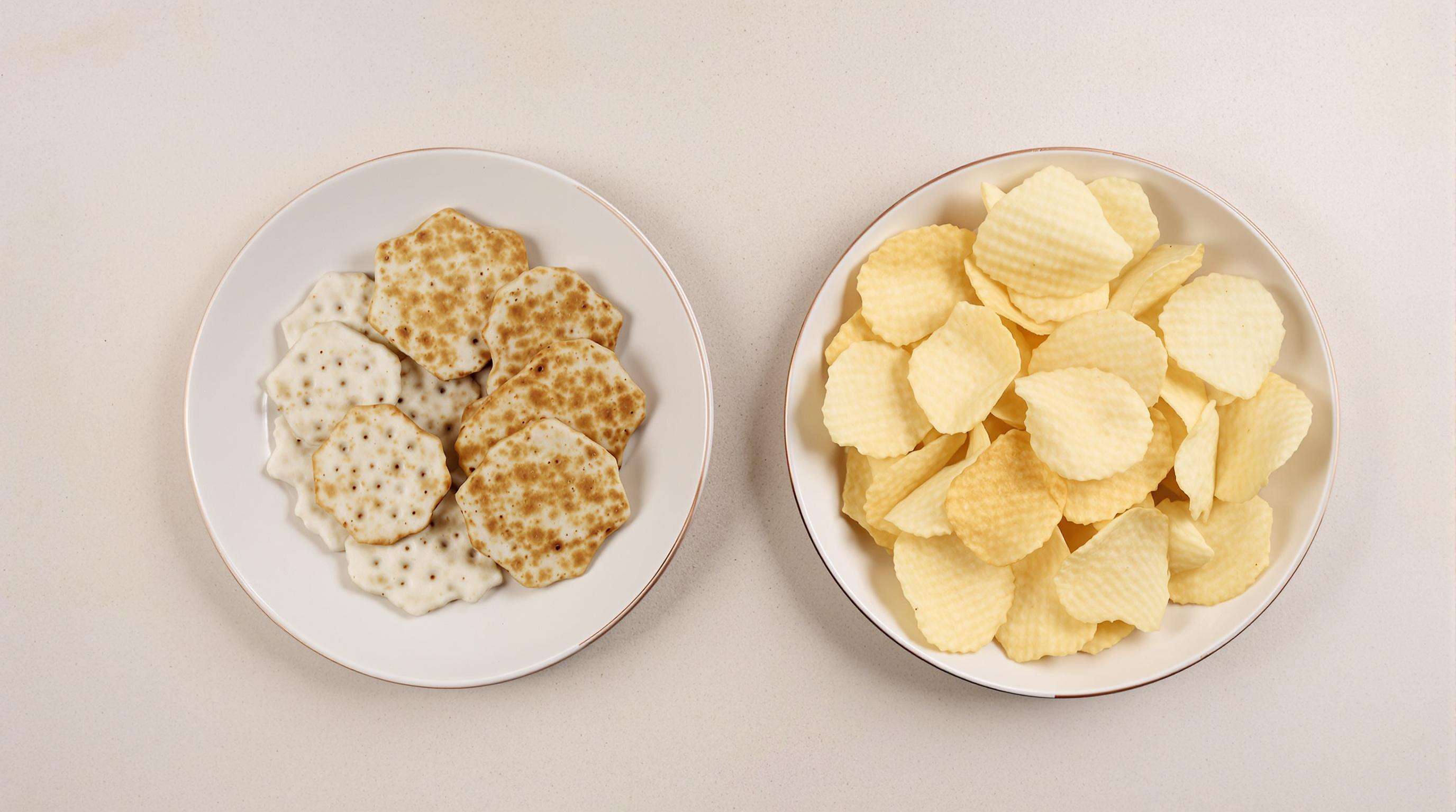 A plate of senbei rice crackers next to a plate of potato chips, showcasing their distinct textures and colors