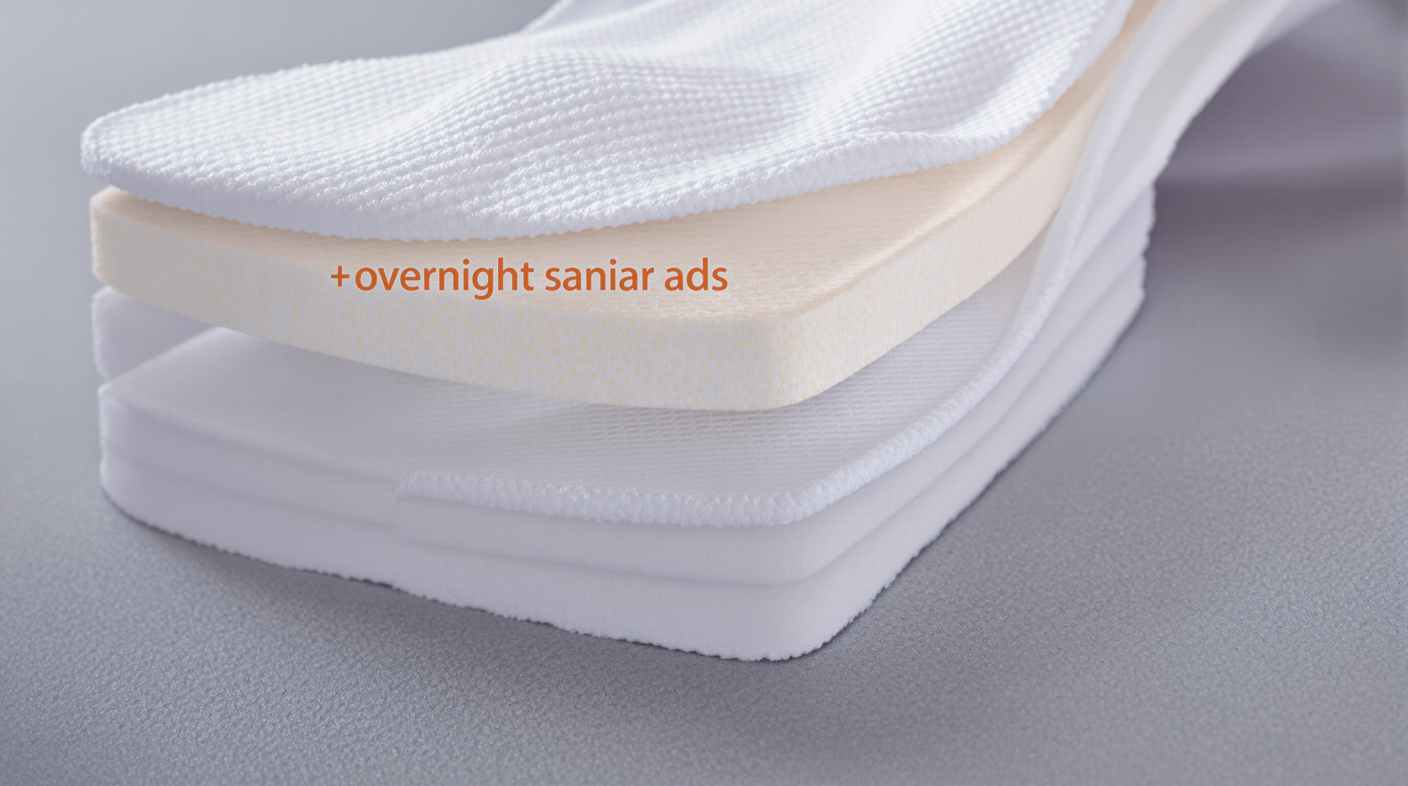 Cross-sectional close-up of an overnight sanitary pad showing layered core and fluid channels