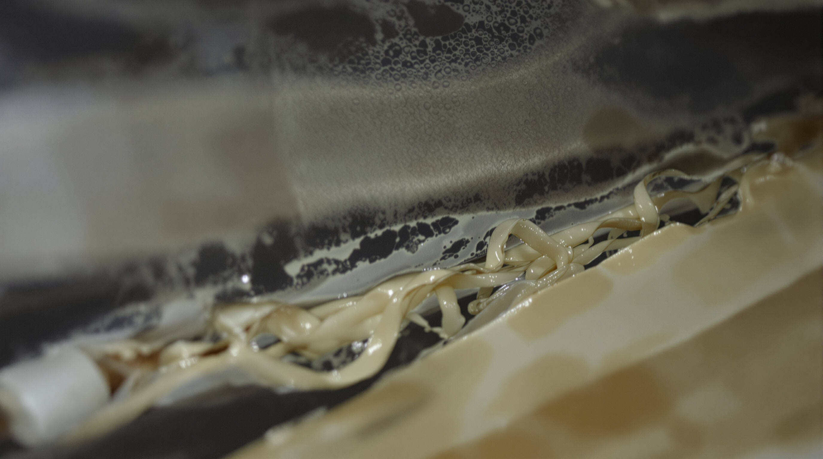Close-up of adhesive strips degrading in a lab oven, showing melting polymer and condensation