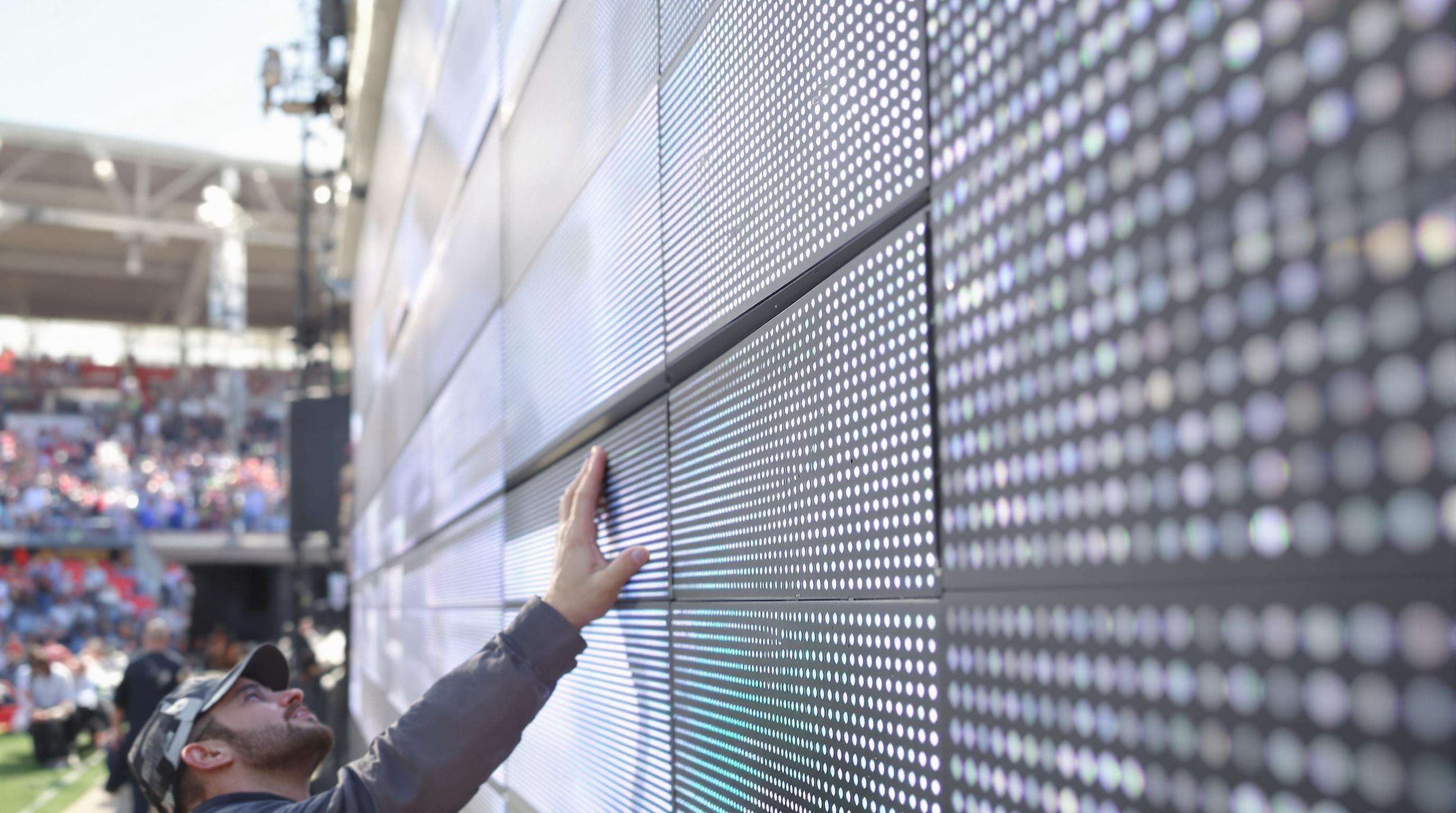 Technician inspecting a large outdoor modular LED screen at a daytime event