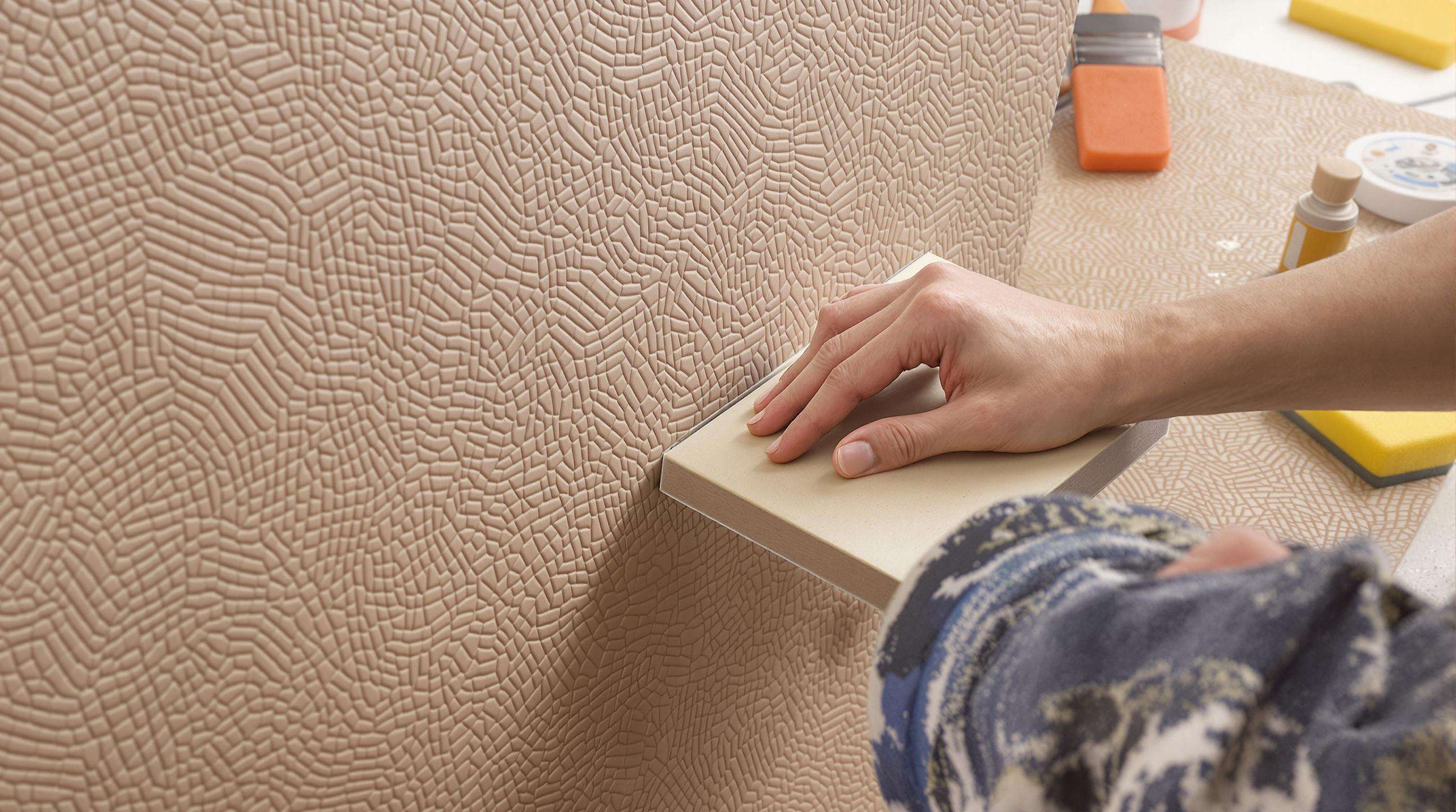 Close-up of hands embossing and stamping textured patterns onto an artificial leather wall panel with tools.