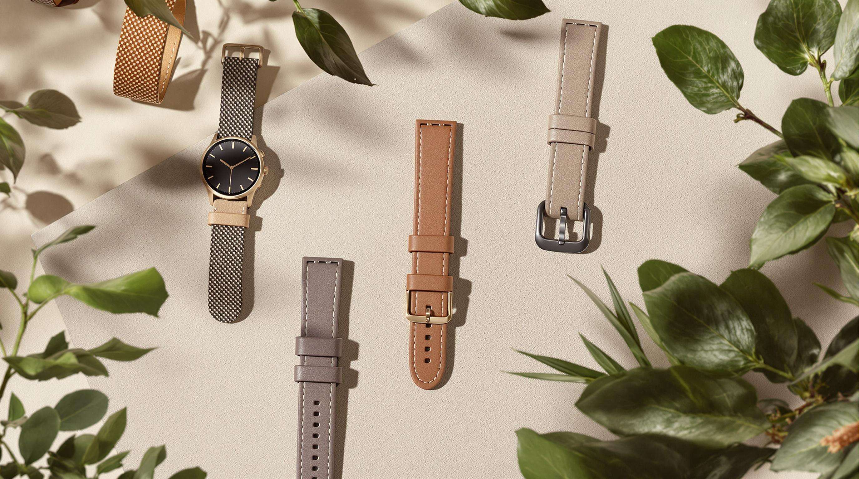 Various wearable devices made of bio-fabricated and plant-based leathers displayed on a soft surface with natural elements, highlighting sustainable materials in smart wearables.