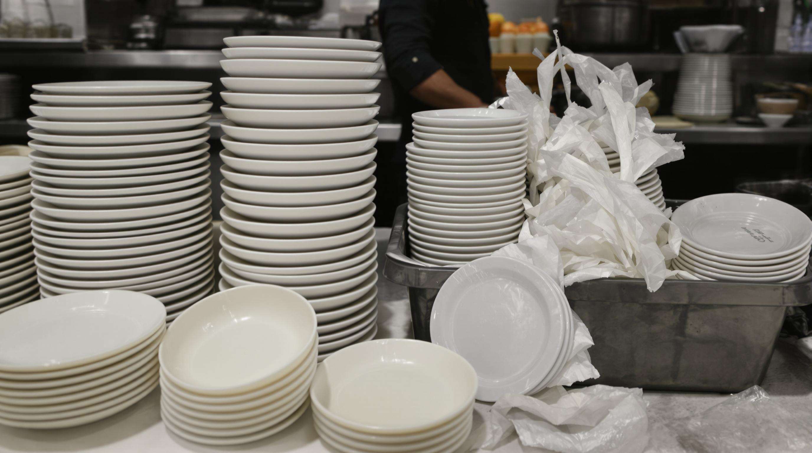 Reusable ceramic sushi plates being stacked beside discarded plastic plates in a kitchen, emphasizing sustainability