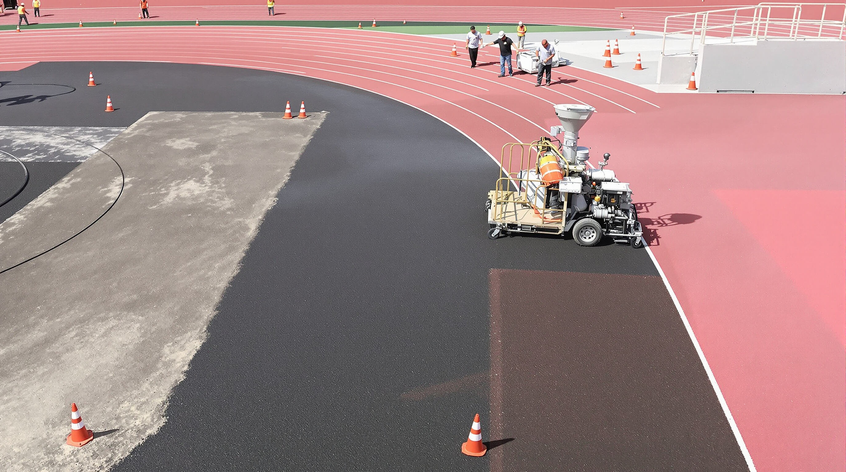Workers resurfacing a running track using specialized equipment, showing contrasting old and new track sections