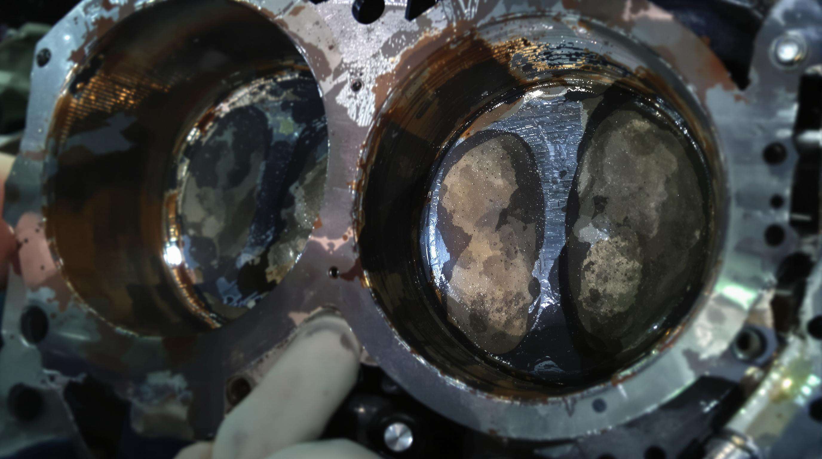 Close-up view of a used engine cylinder liner displaying distinctive wear marks and scoring, inspected by a mechanic.