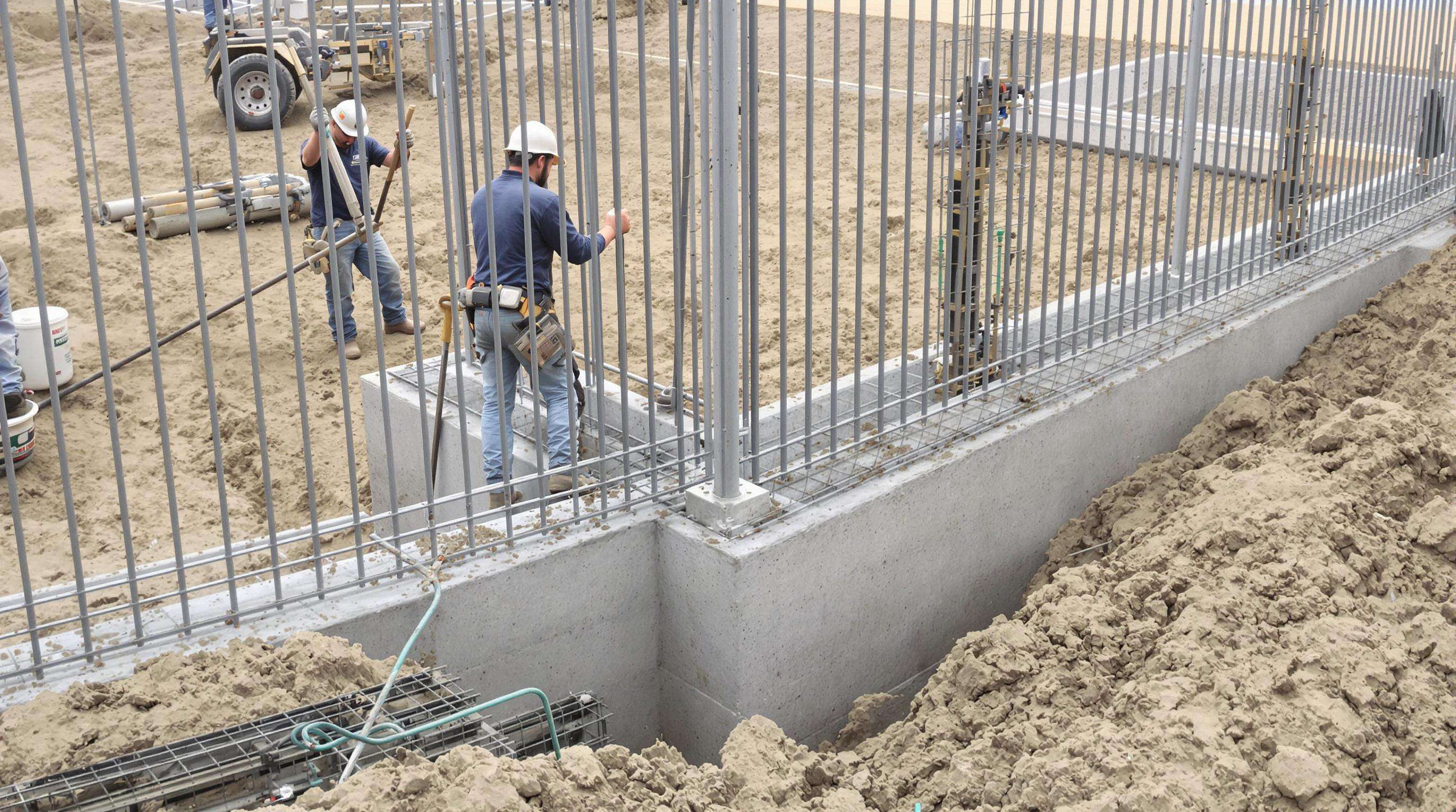 Workers installing fence posts and concrete foundations for stable perimeter fencing