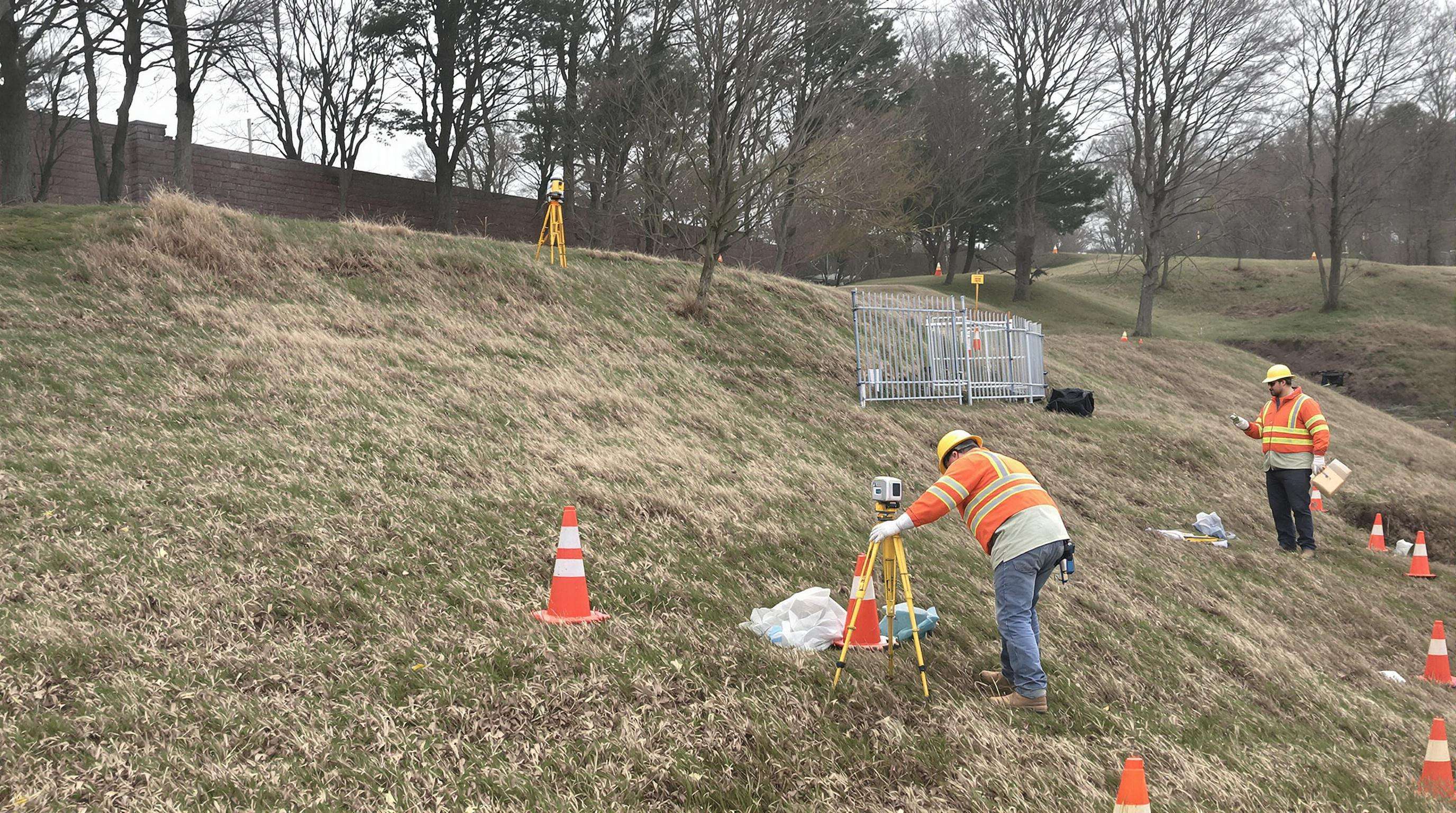 Surveyors performing layout mapping for fence installation on uneven terrain