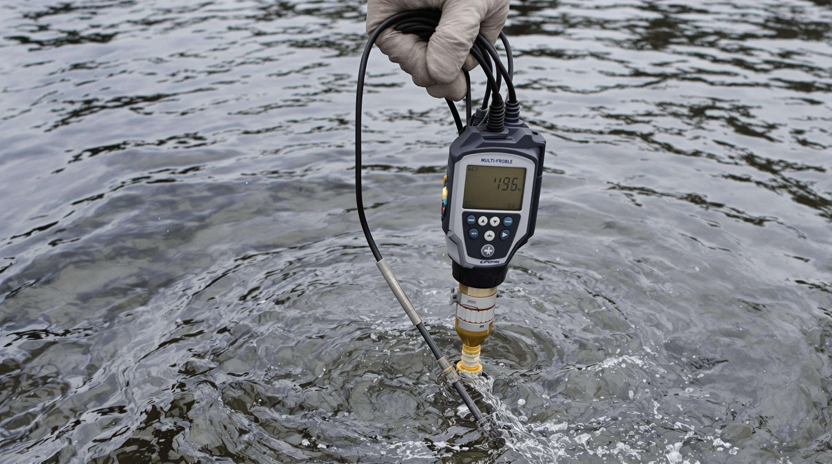 Scientist using a portable water quality sensor in a river to measure temperature and conductivity
