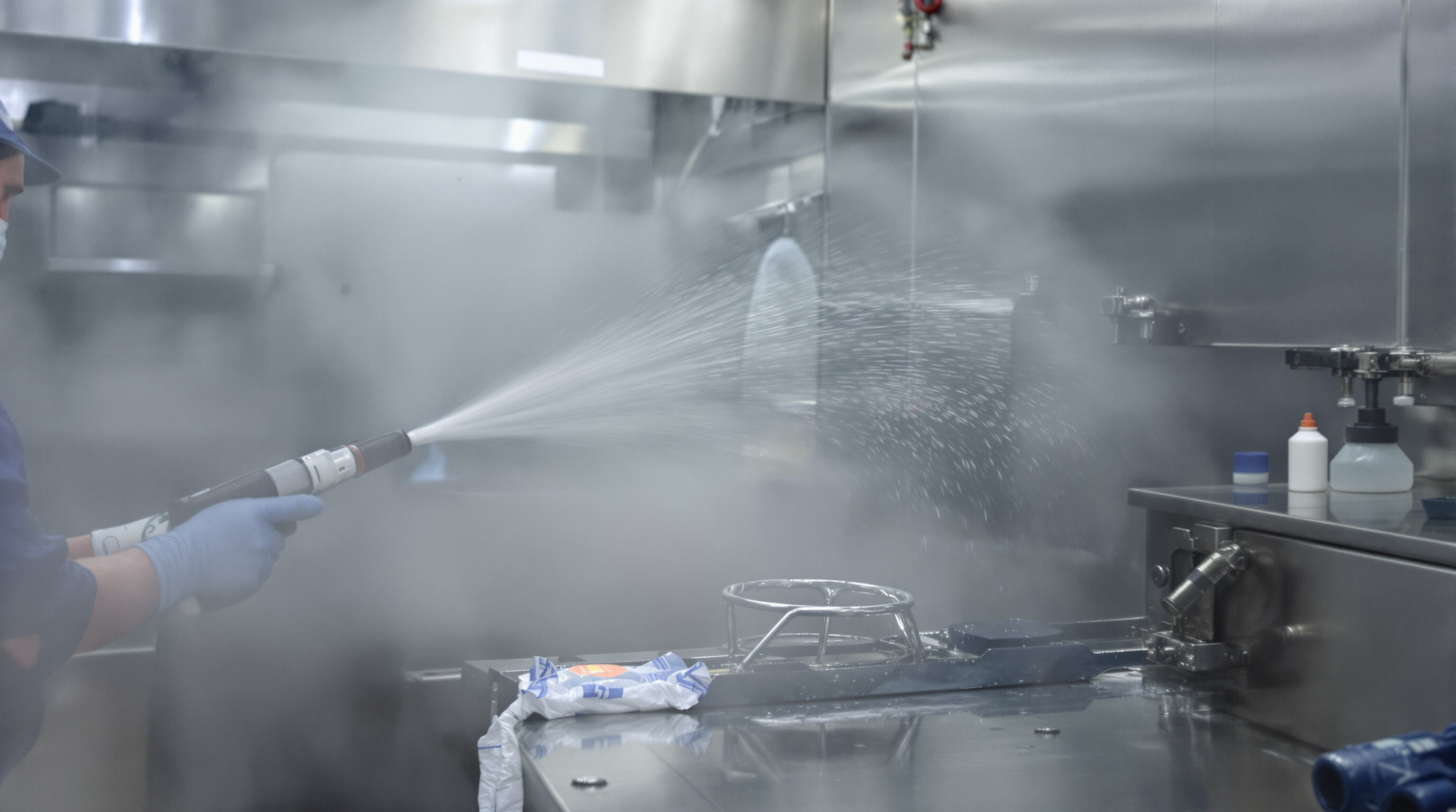 Worker cleaning stainless steel meat processing equipment with sprayers and foam, focusing on key mechanical areas