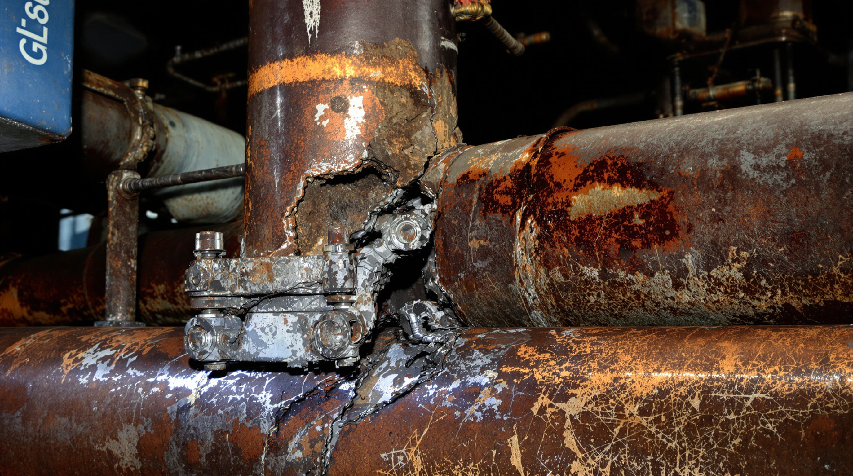 Corroded and cracked pipe weld close-up showing porosity and misalignment in an industrial environment