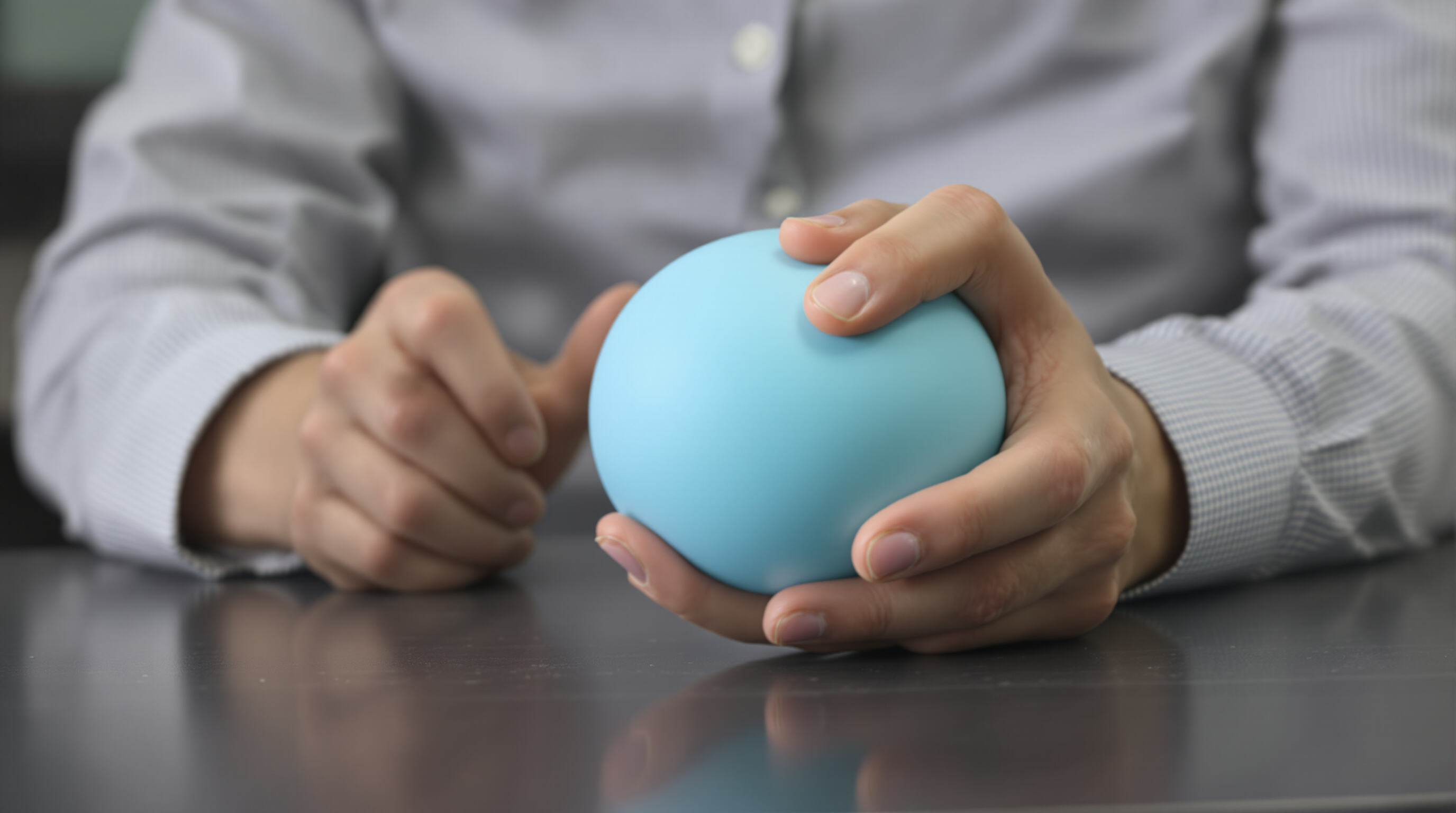 A close-up photo of a hand squeezing a stress ball in an office setting, emphasizing tactile stimulation and a sense of calm.