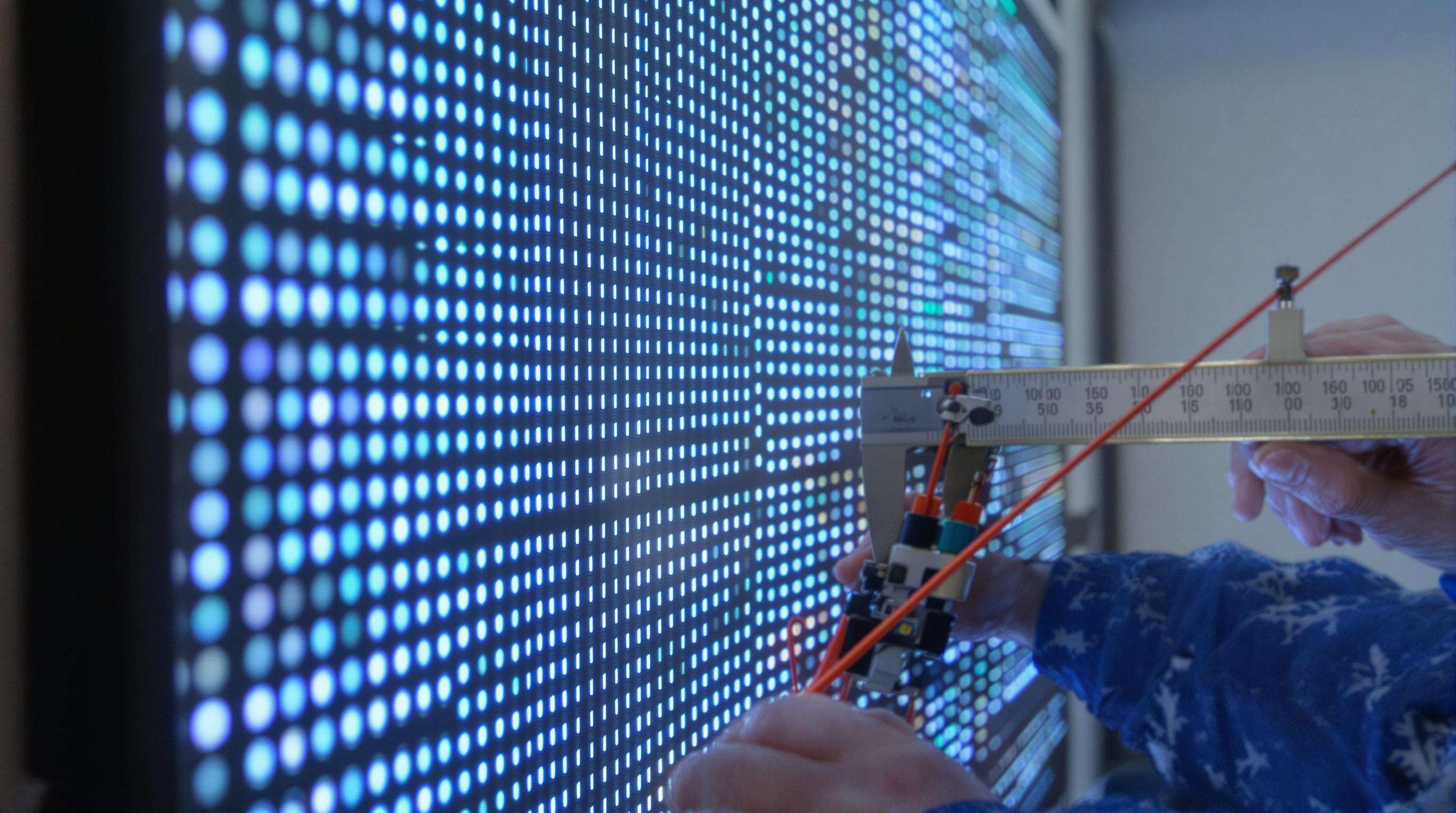 Technician measuring LED pixel pitch on a screen wall with calipers
