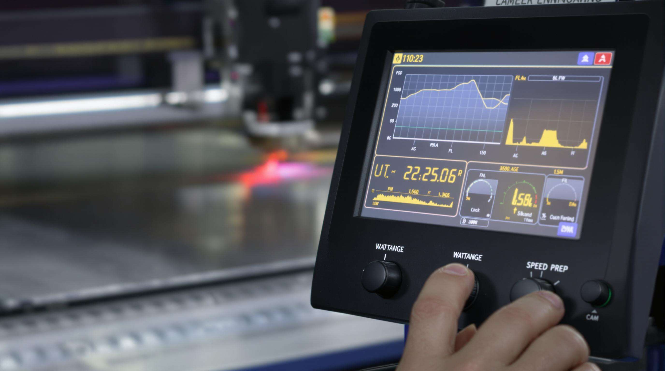 Close-up of a laser machine control panel with hand adjusting power and speed controls, machine working on metal in the background