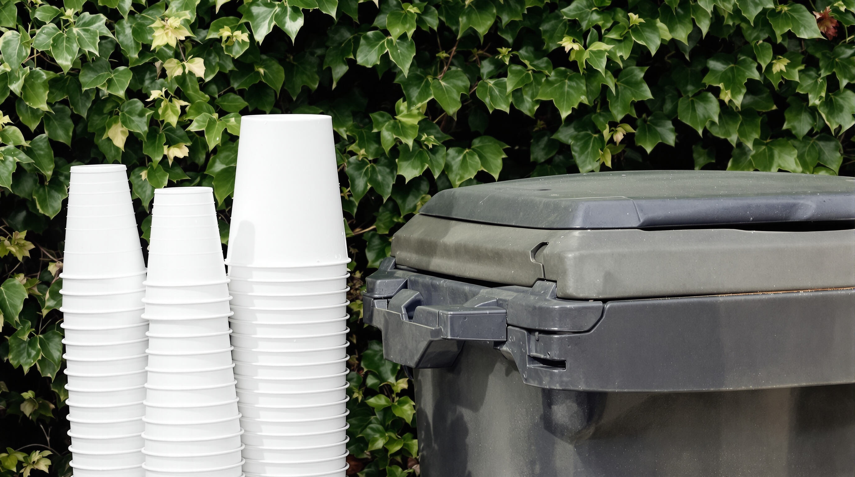 Stack of reusable plastic yard cups next to a recycling bin outdoors highlighting sustainability