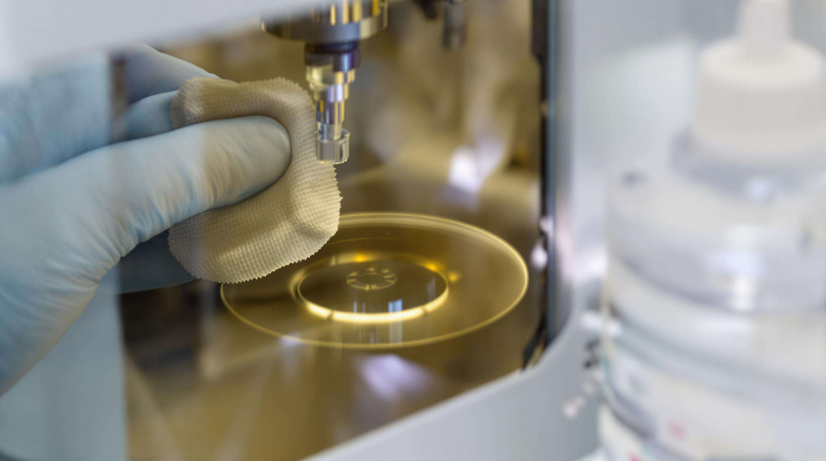 Technician carefully cleaning a laser lens with a lint-free wipe under angled lighting