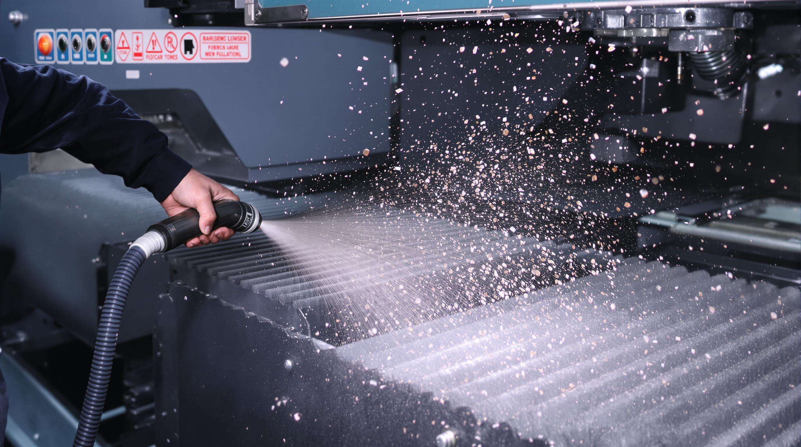 Person using compressed air to clean dust from metal radiator fins on an industrial laser machine