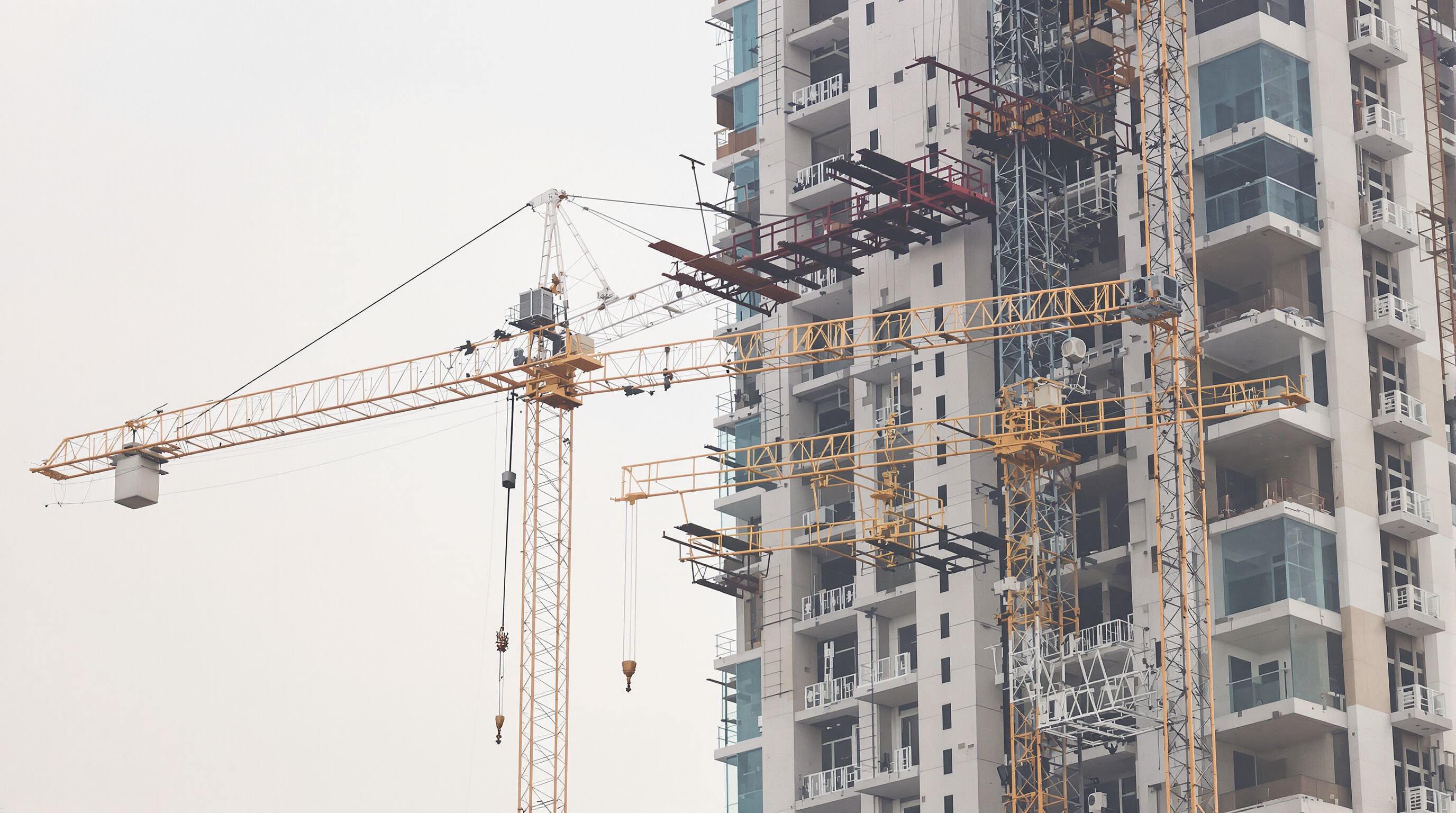 A gantry crane moving steel beams and concrete panels on a tall building construction site