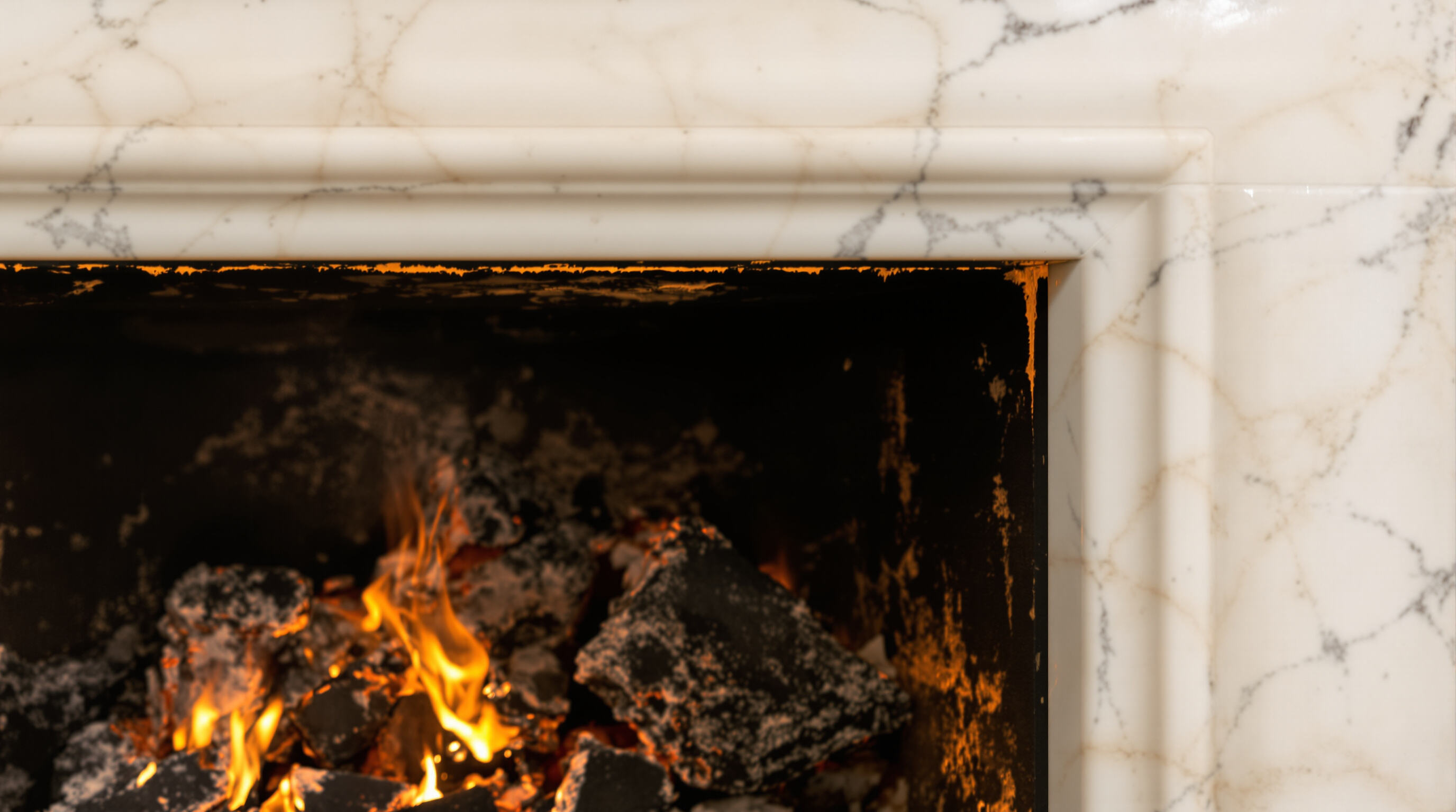 Close-up of a marble fireplace enduring active flames, showing its sturdy surface and intact veining