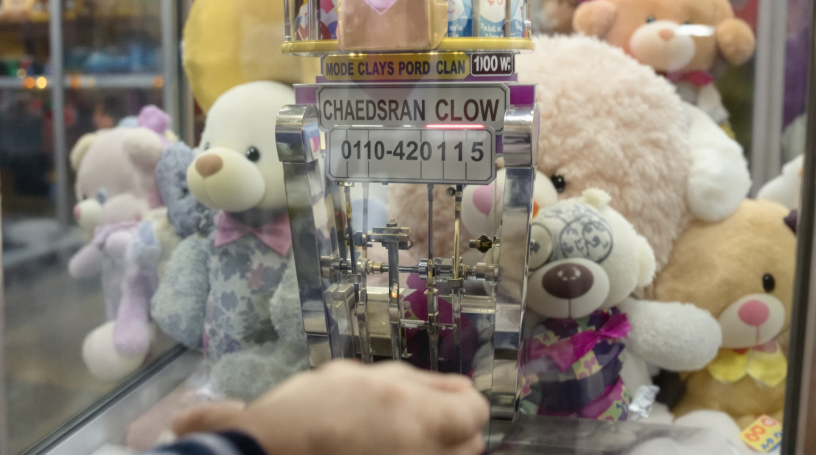 Close-up of a child's hand on a joystick as the claw arm descends toward prizes inside a claw machine.