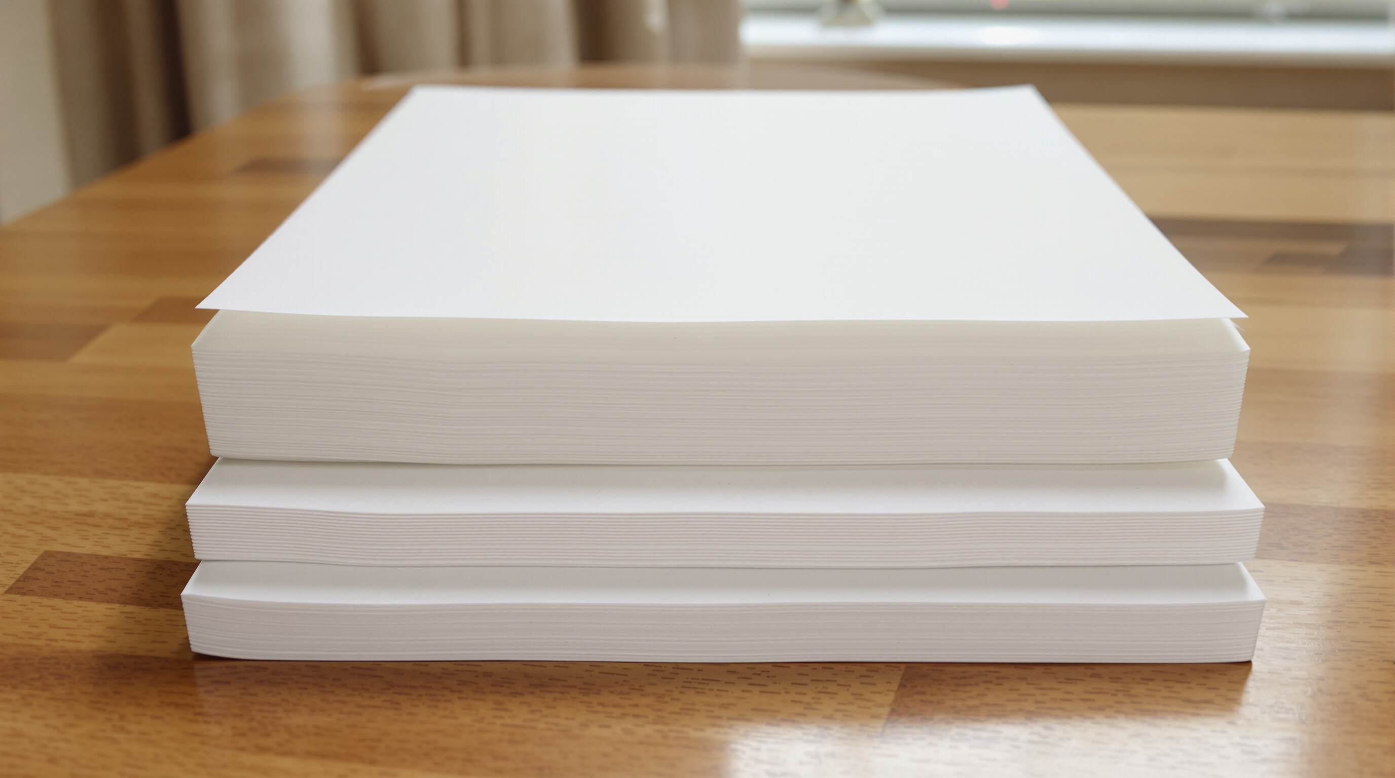 Three Bible paper samples—ultra-thin, translucent, and textured—stacked on a wooden surface