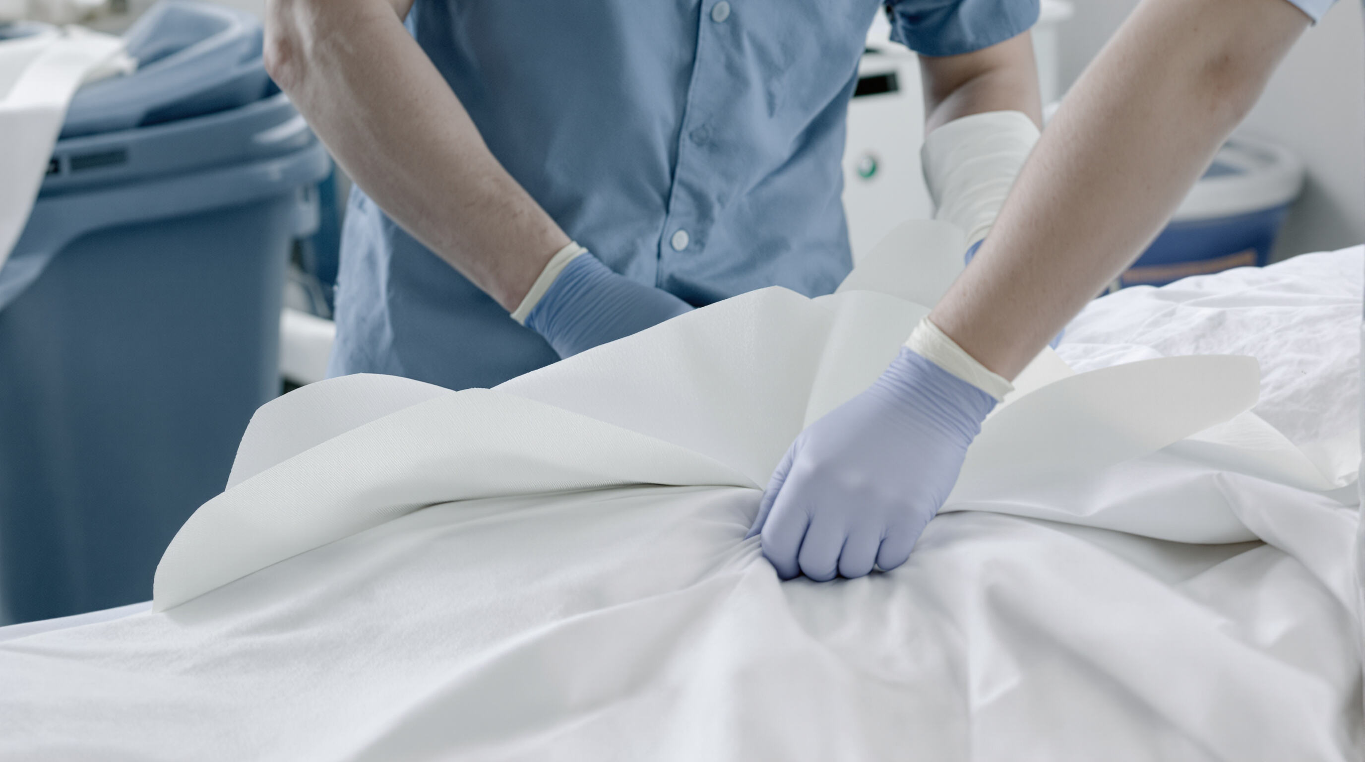 Healthcare worker removing used disposable sheet from patient bed in a hospital room, showing infection control practices
