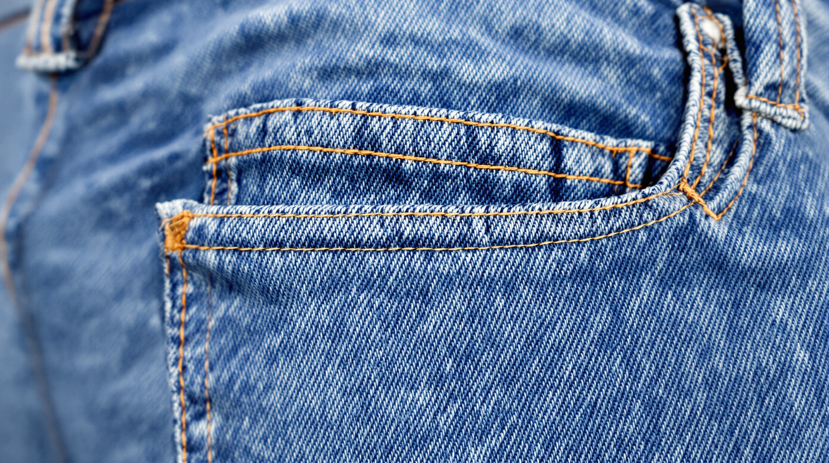 A detailed close-up of stretch denim fabric showing seams and pocket corners, highlighting its weave and core-spun yarn structure
