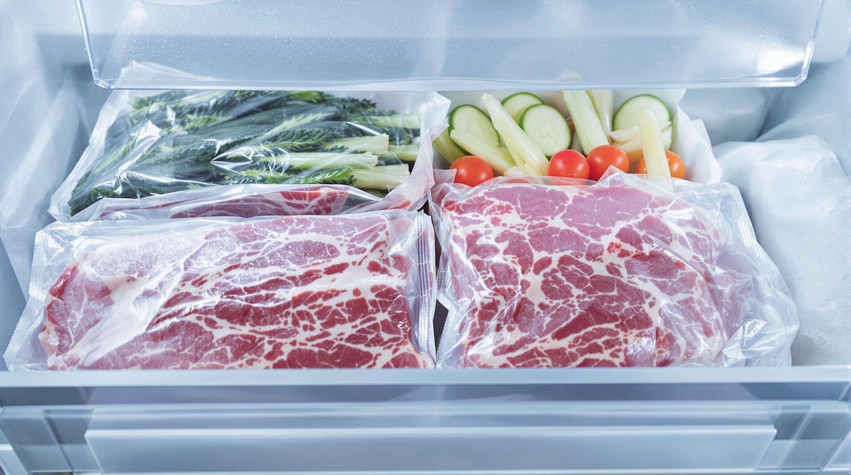 Vacuum-packed frozen steak and vegetables in a freezer with minimal ice crystals
