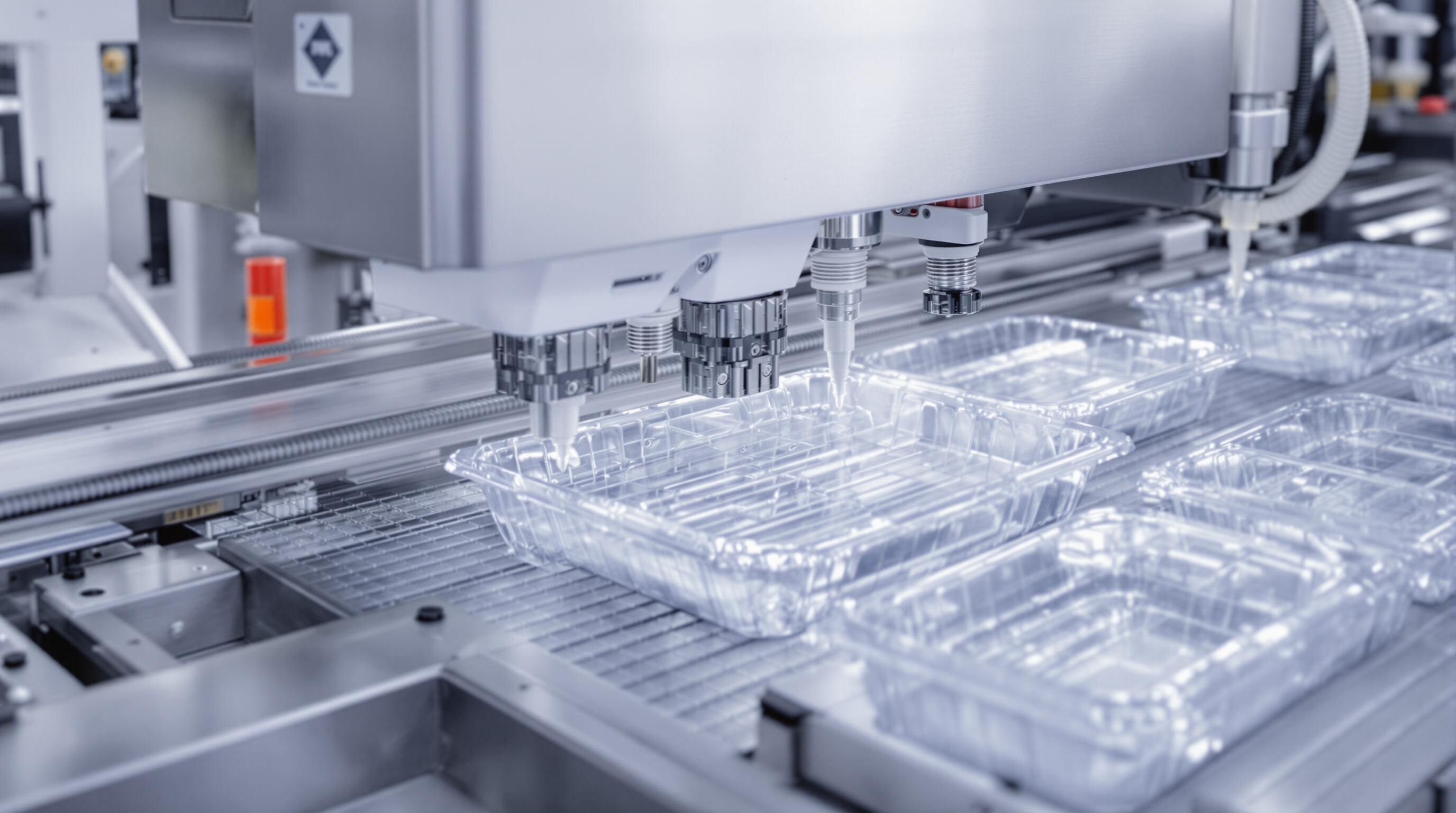 Close-up of a tray sealing machine applying a seal with modified atmosphere packaging in a food factory.