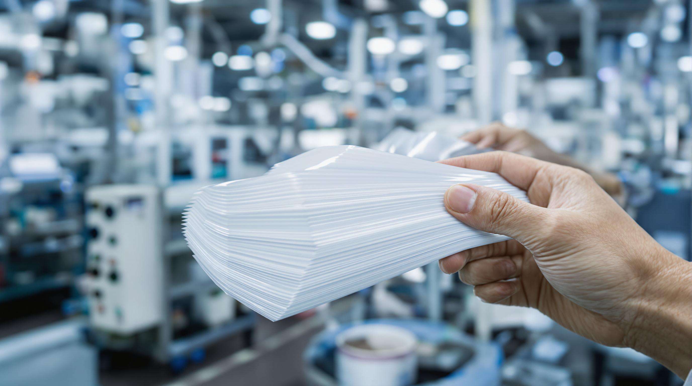 Hands holding advanced multilayer packaging films with visible layers in a food packaging factory.