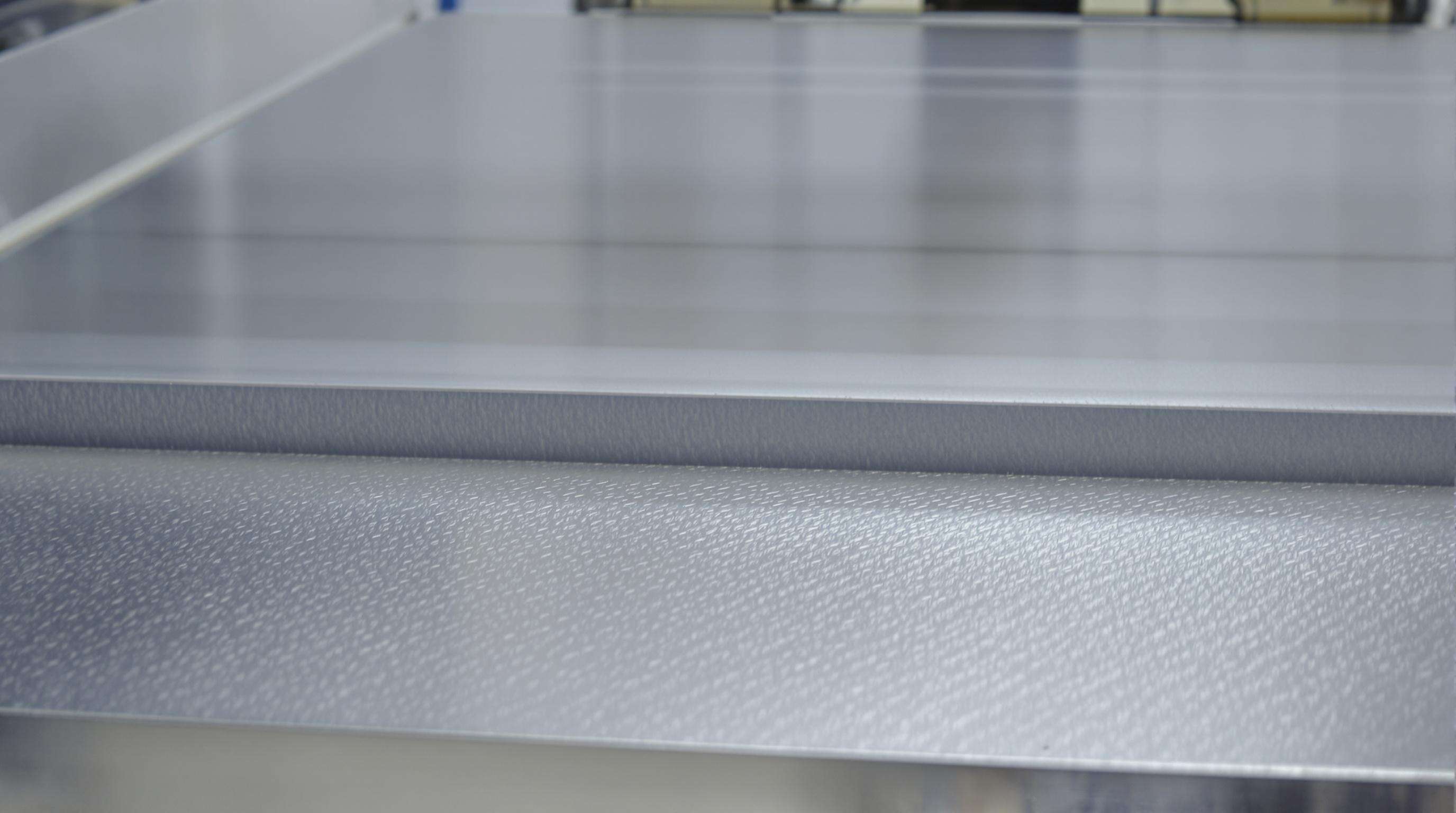 Close-up of metal sheet with fine sanding marks from wide belt sander in an industrial setting, prepared for coating