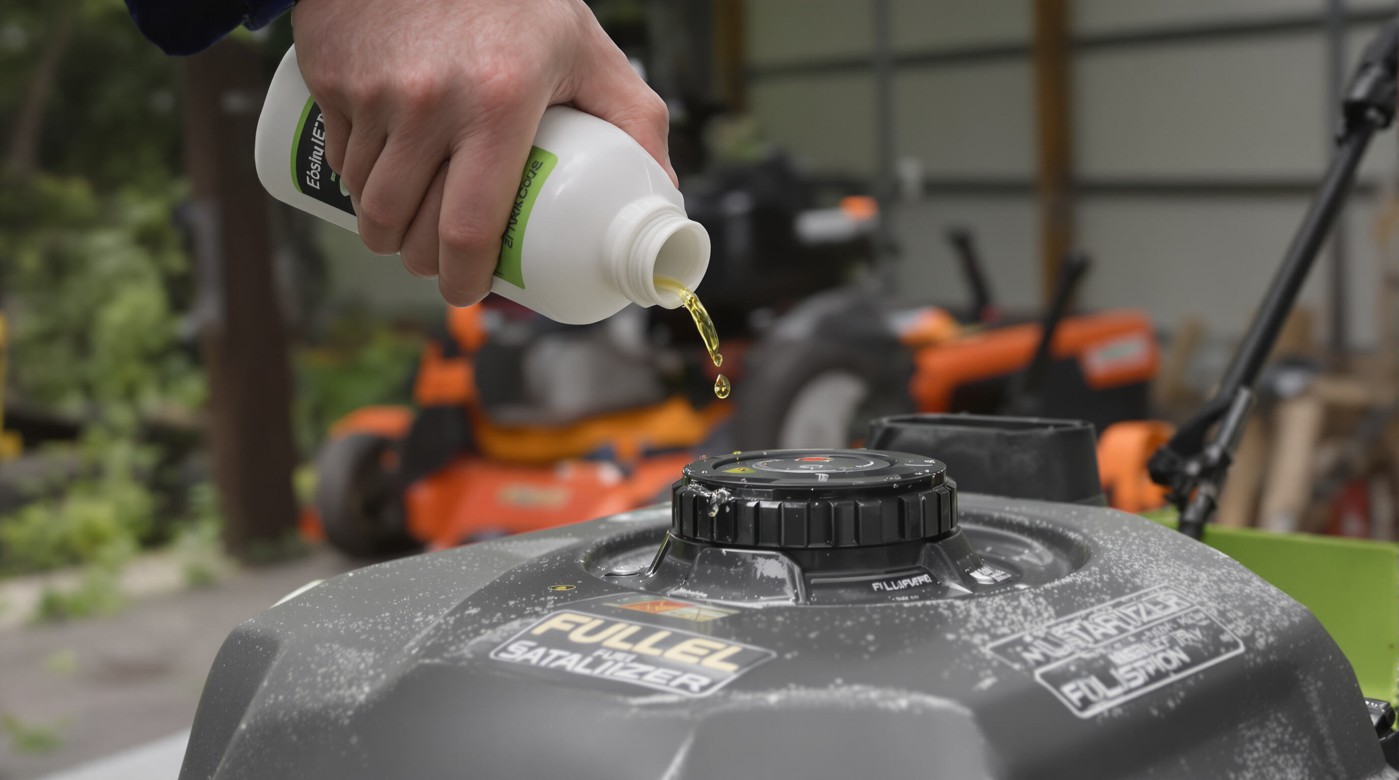 A person adding fuel stabilizer to a gasoline lawn mower's tank in a shed