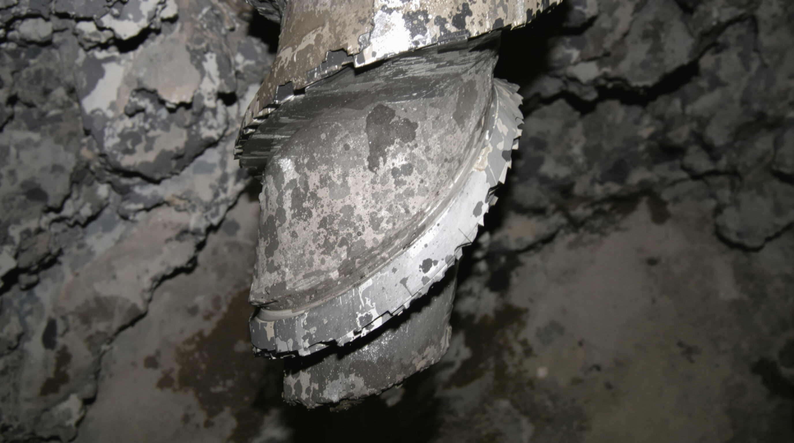 Close-up realistic photo of a damaged tricone drill bit showing wear, debris, and signs of overheating.