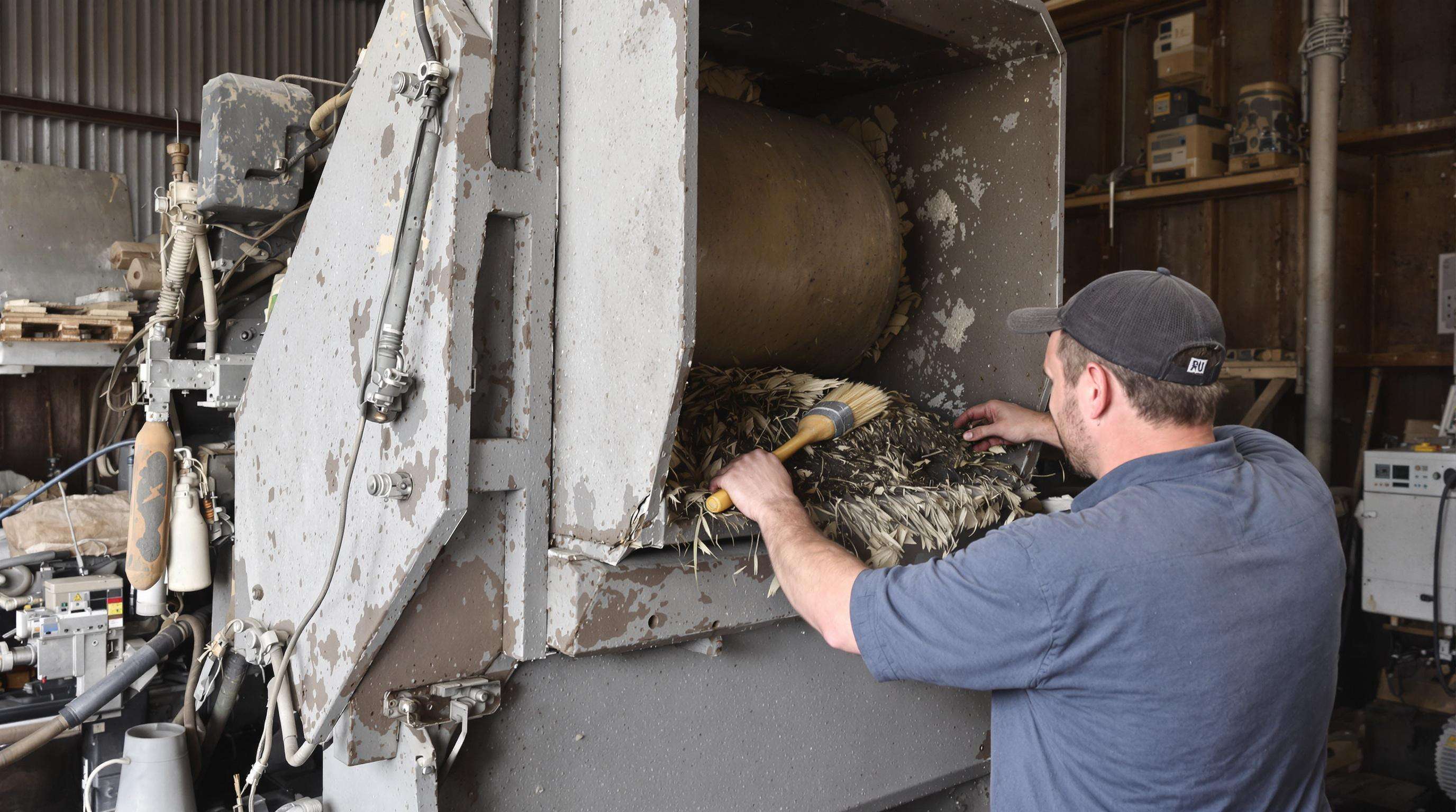 Technician cleaning and inspecting a chipper shredder in a workshop environment