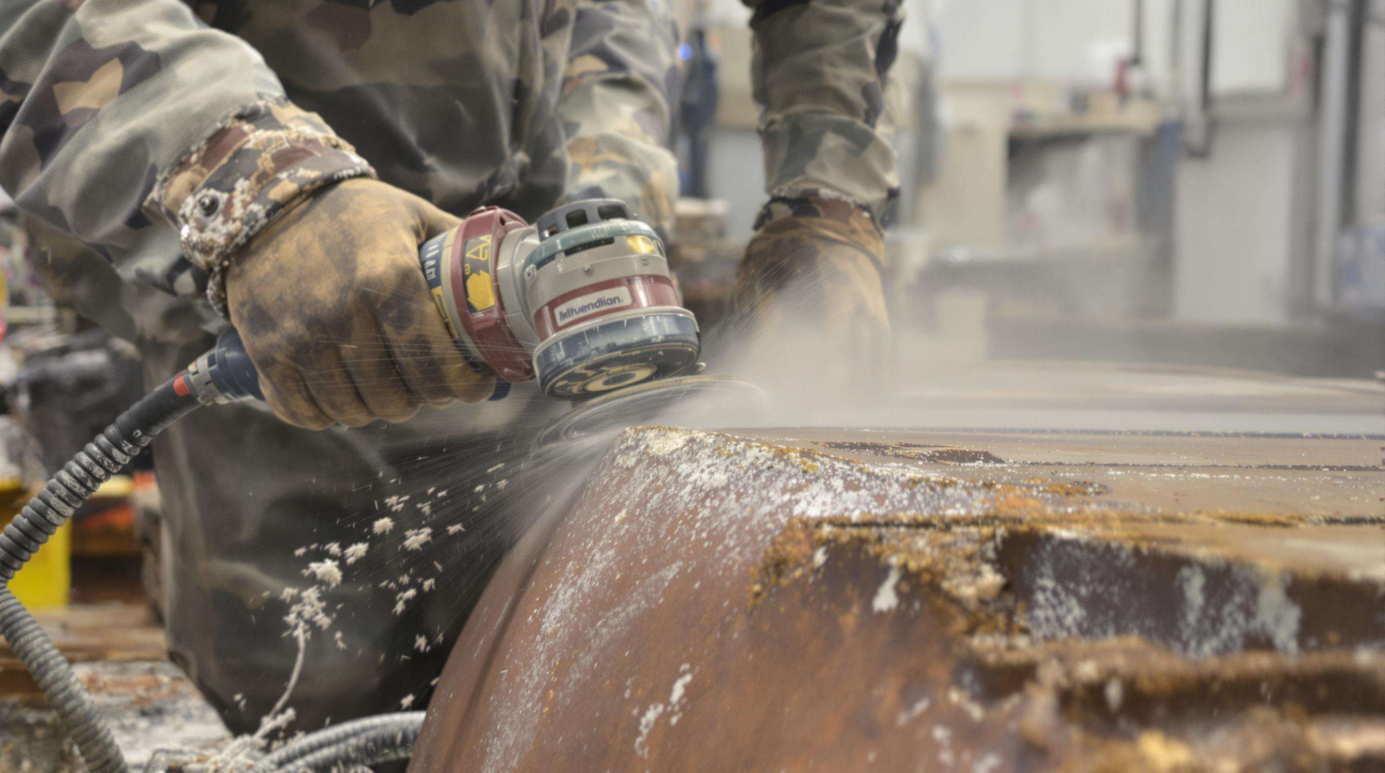 Technician grinding metal surface to prepare for hardfacing welding in a workshop