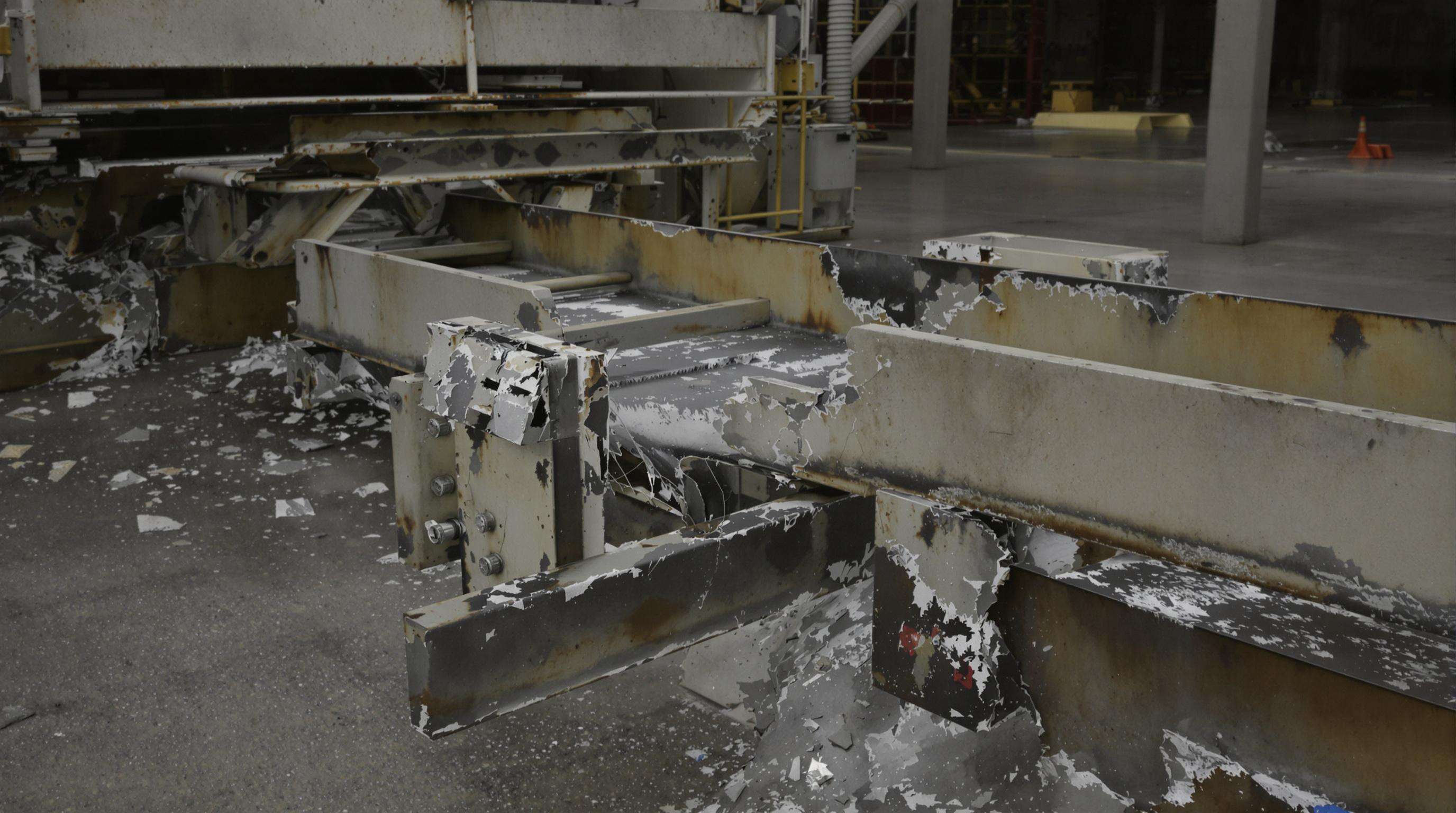 Industrial conveyor system with visibly worn and cracked CCO plates amid scattered abrasive material