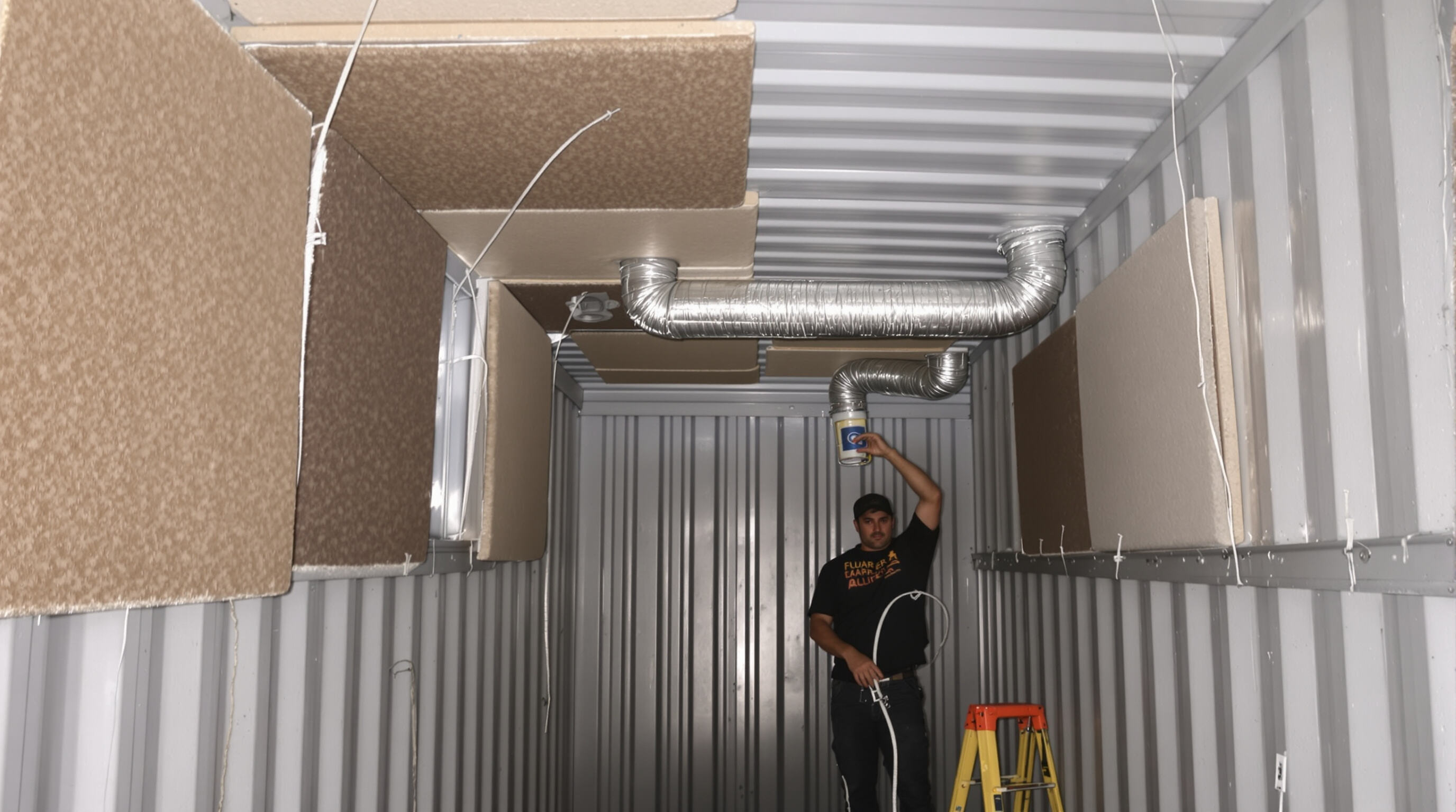 Technician installing soundproofing and ventilation inside a container film set